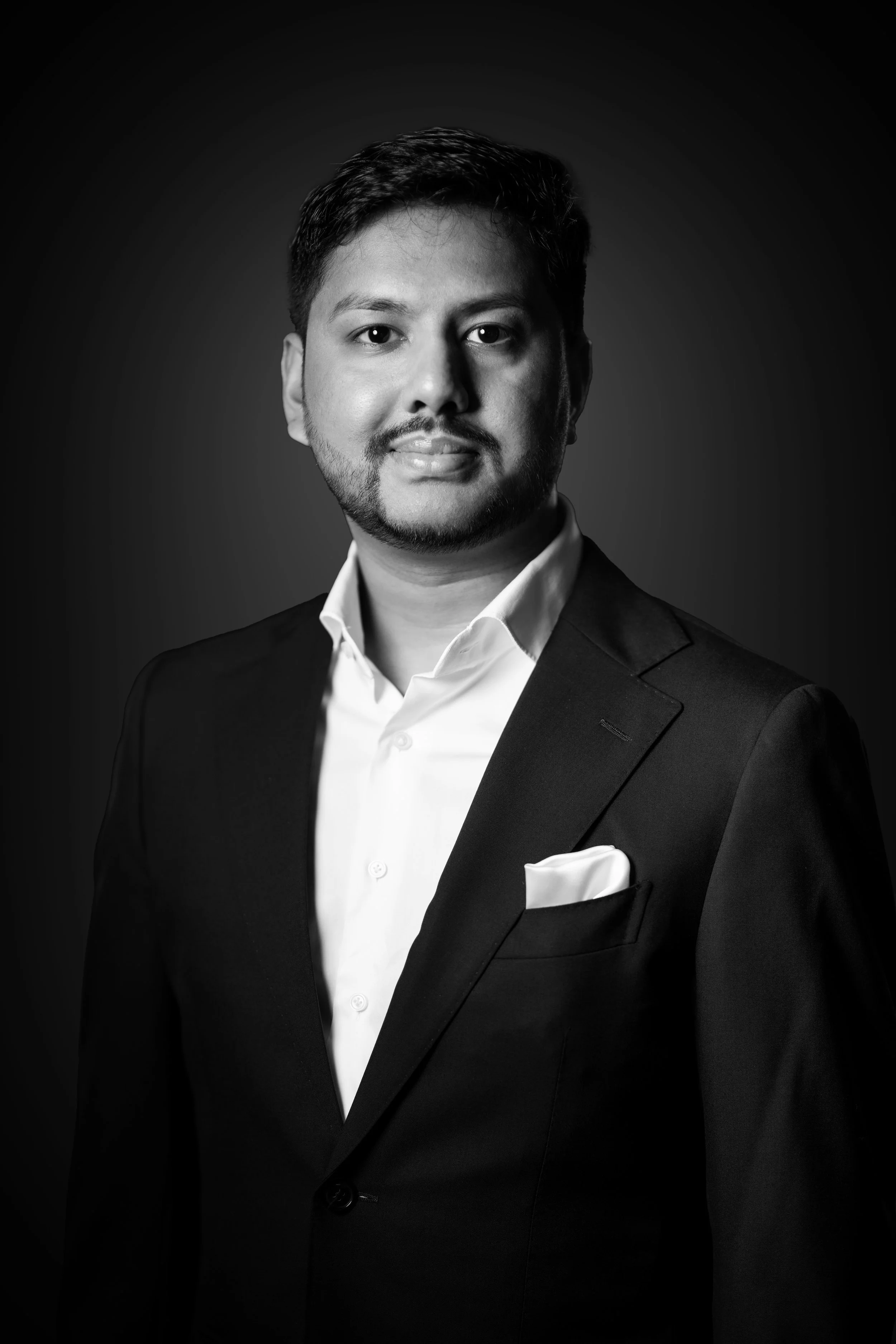 Black and white portrait of a man in a suit with a white shirt and pocket square, looking at the camera with a neutral expression.