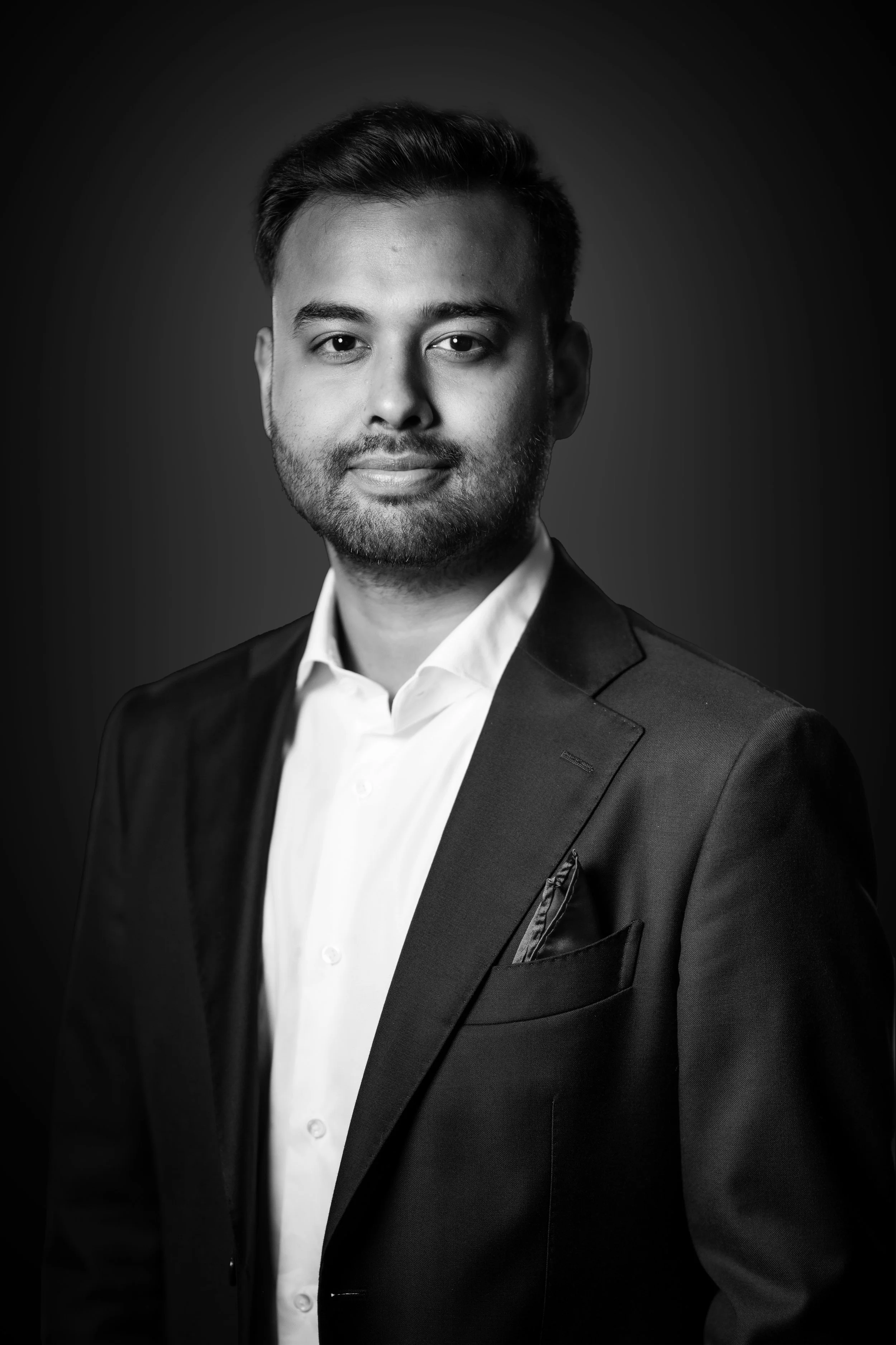Black and white portrait of a man wearing a formal suit with a white shirt, looking directly at the camera with a slight smile.