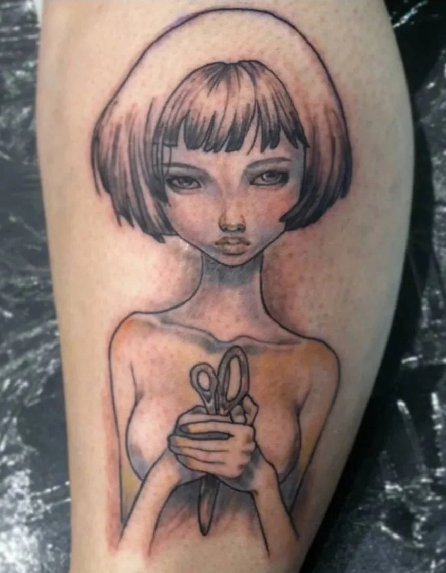 Tattoo of a young girl with short hair, holding a pair of scissors and a cup, with detailed facial features and a simple background.