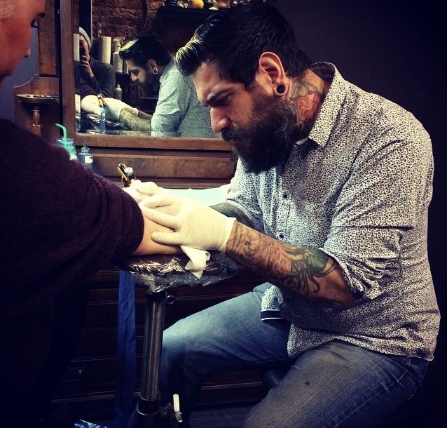 Man with tattoos getting a tattoo on his arm at a tattoo parlor.