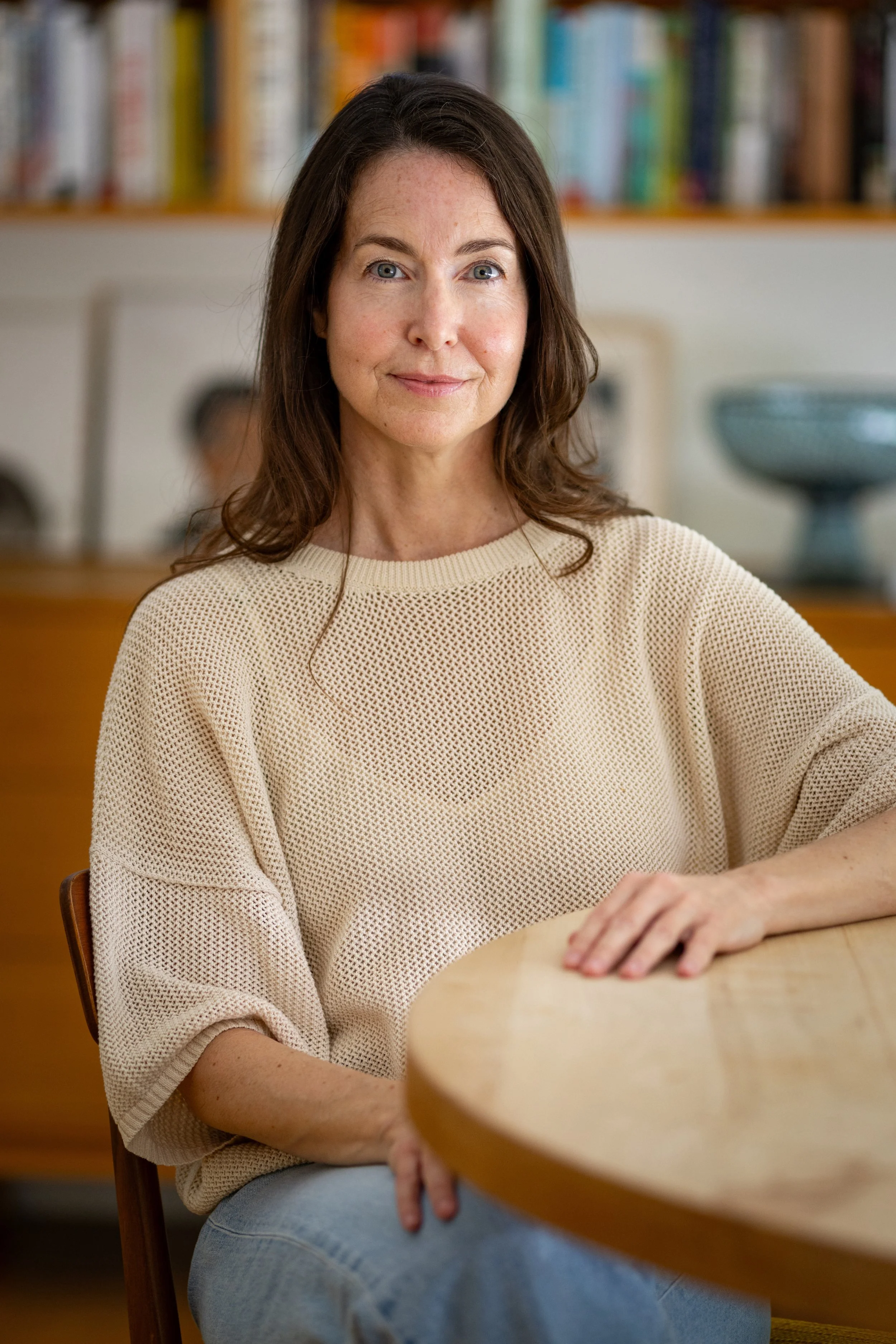 Erin Russ, author of Becoming the Ocean: A Memoir, is sitting at her kitchen table with blurred images of books behind her.