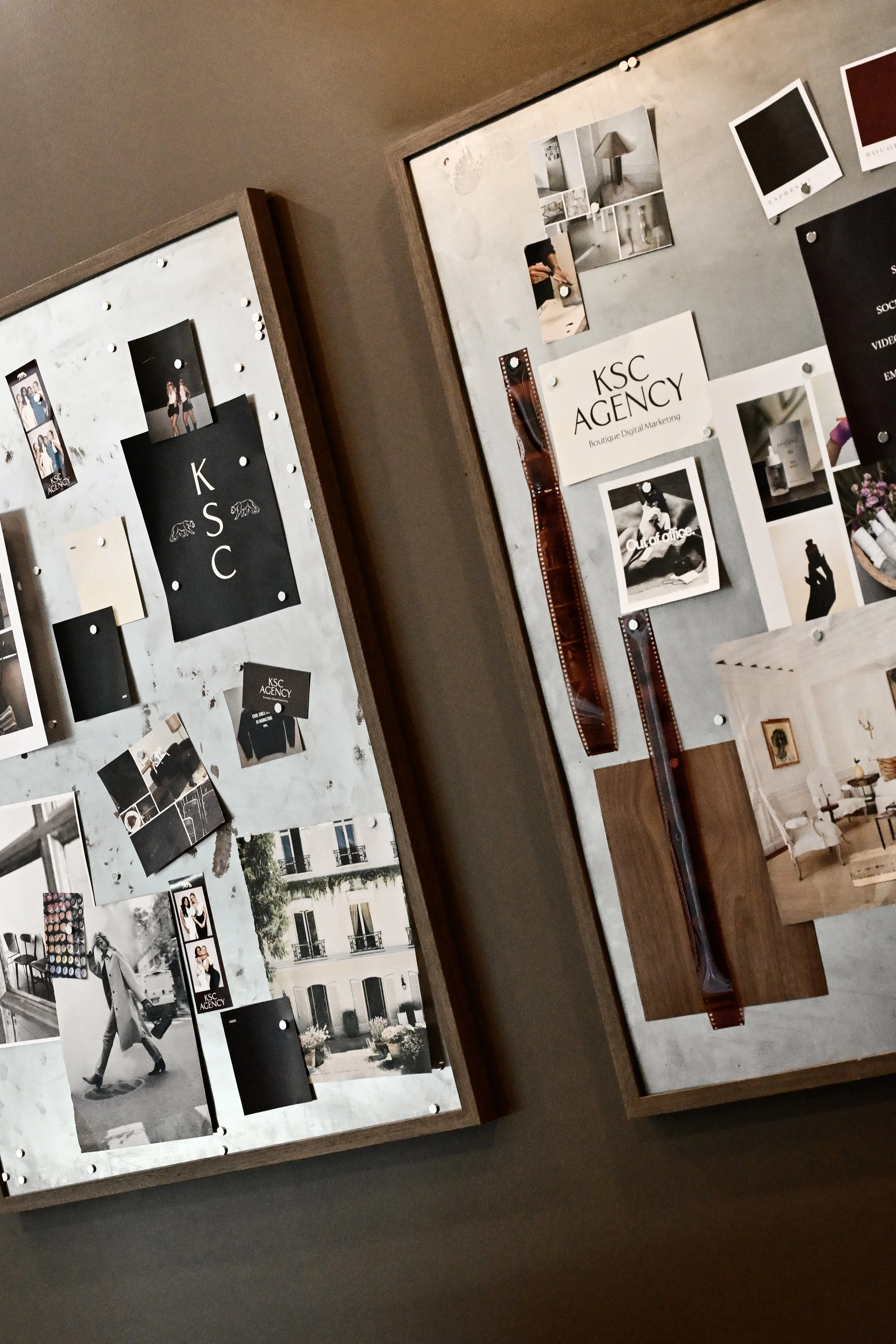 Photo of a bulletin board showcasing various black and white and color photographs, posters, and printed materials related to KSC Agency, a boutique digital marketing company. The display includes images of people, cityscapes, and products, with some photographs attached directly and others pinned on a board with pushpins.