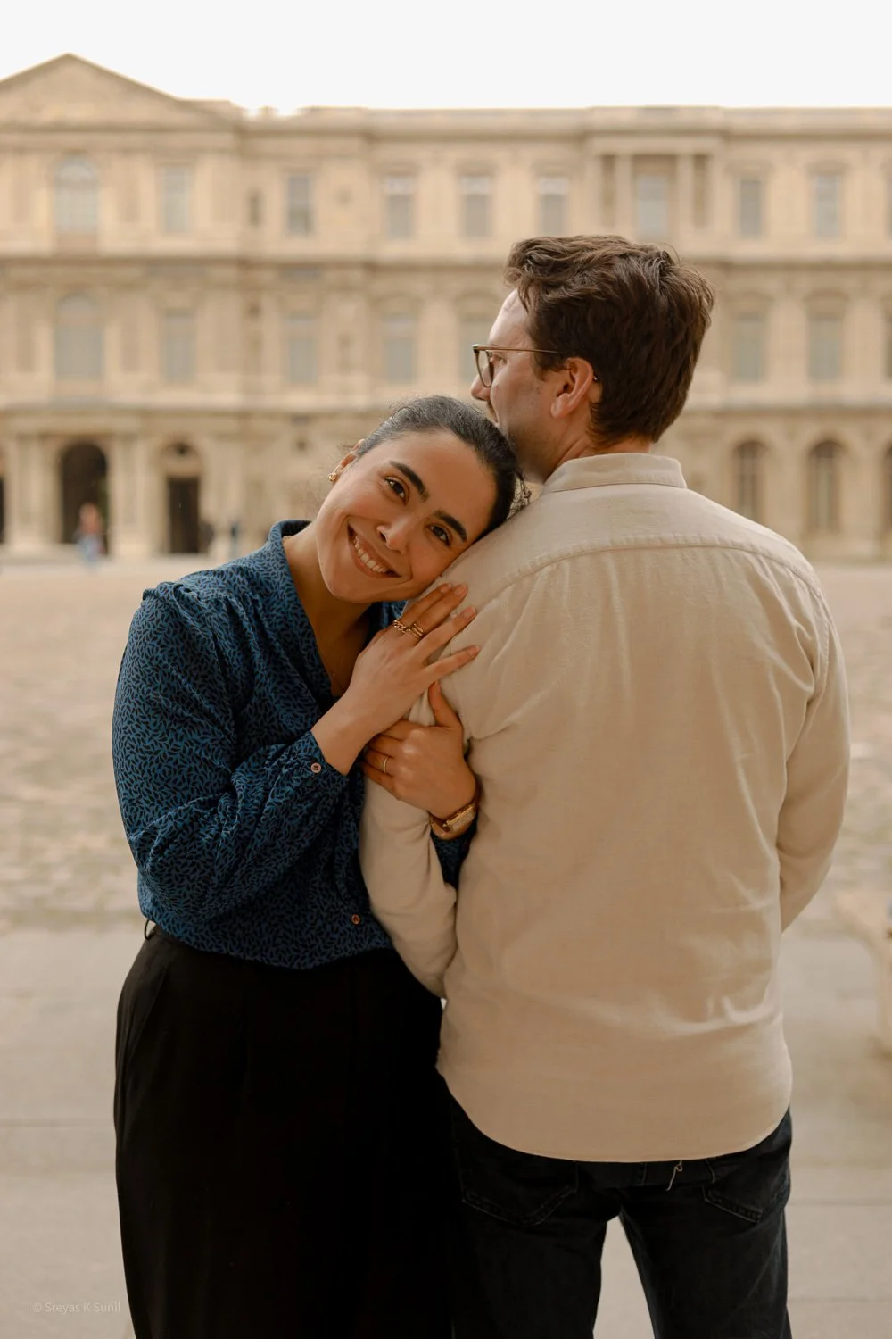 A smiling woman is hugging her man outdoors in front of a historic building.