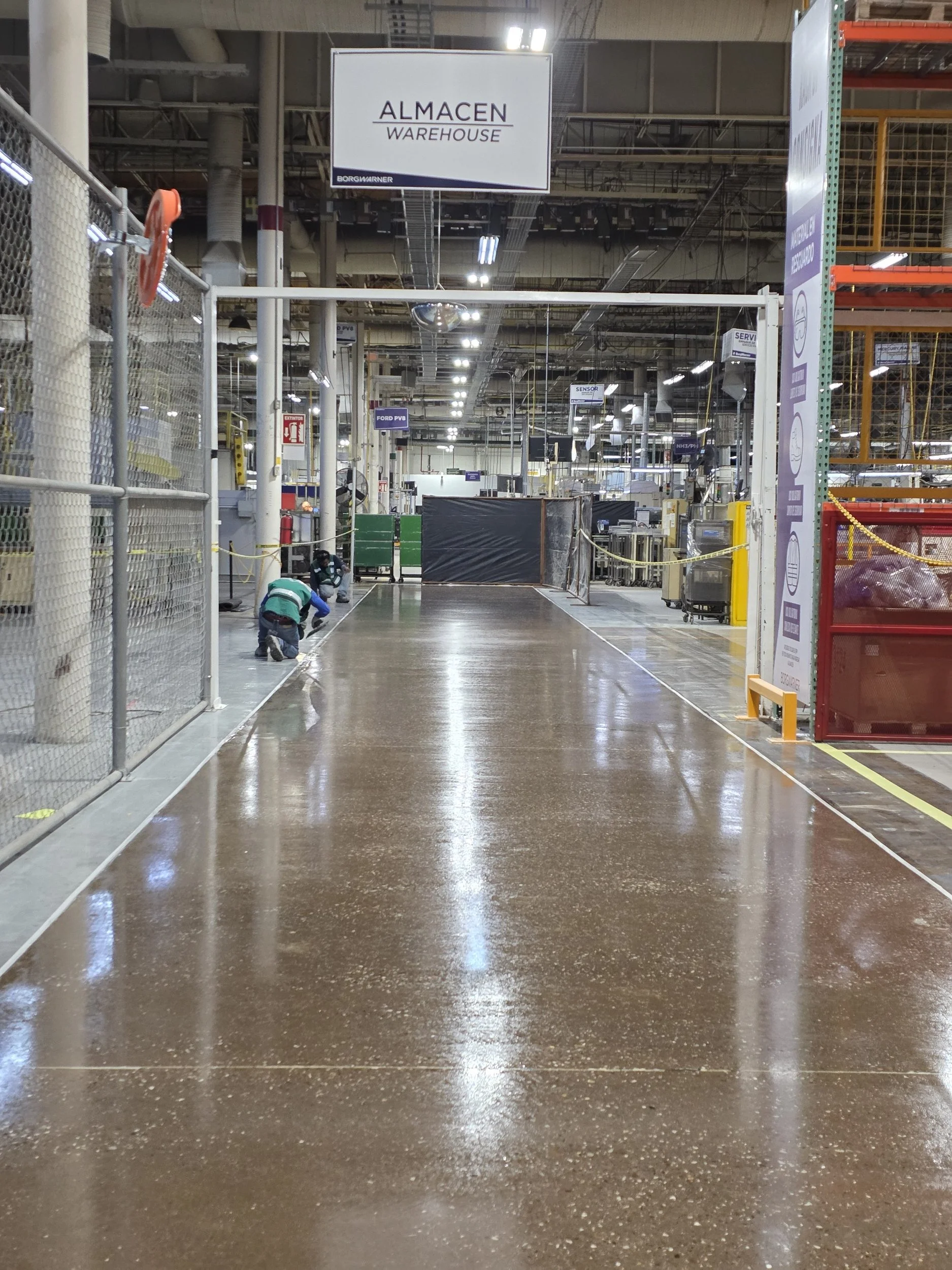 Interior de un almacén, con una señal que dice 'ALMACÉN WAREHOUSE', trabajadores realizando tareas y estanterías en el fondo.
