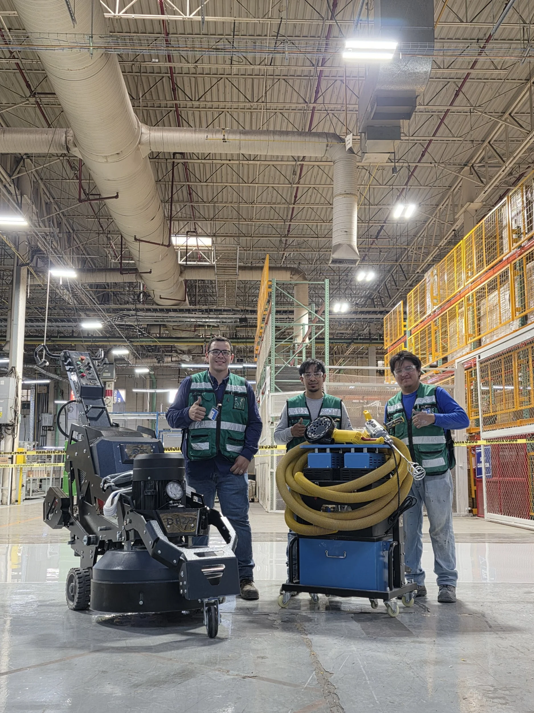 Personal de limpieza con equipo especializado en un almacén industrial, con ventilación y estructuras metálicas en el techo.