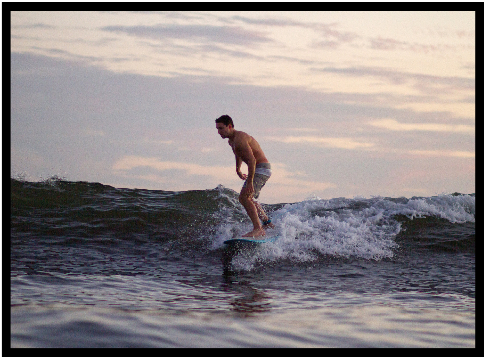 Stan Parish, novelist, journalist and screenwriter surfing on a wave during sunset with a cloudy sky in the background.