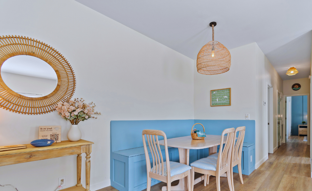 Dining nook at Sol Mar with a round rattan mirror, wooden console table, and blue banquette seating