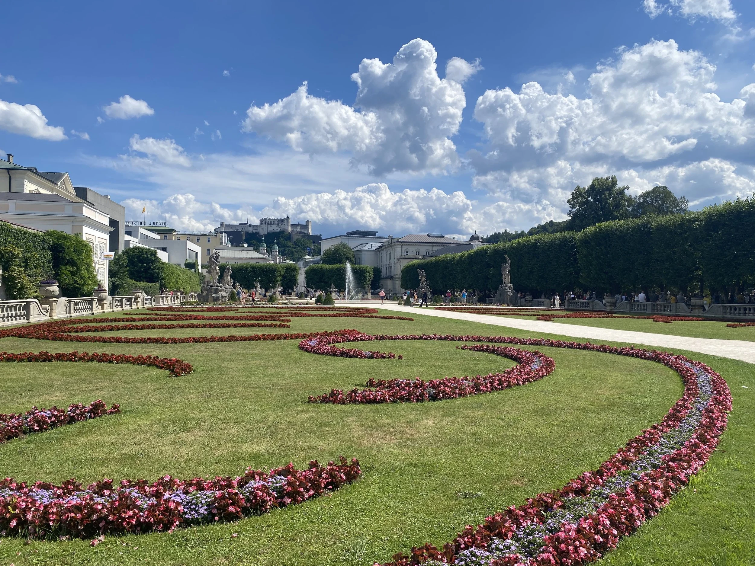 Mirabell gardens with flower beds and manicured lawns, with a historic castle on a hill in Salzburg, Austria