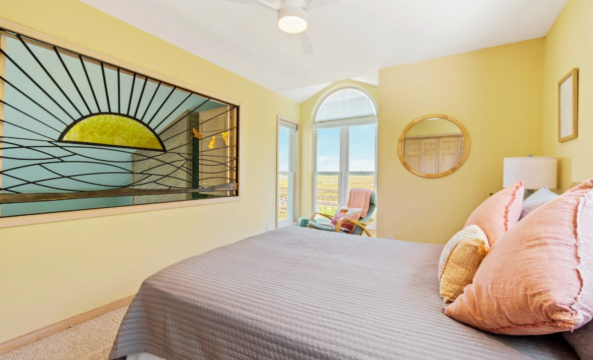 Queen Upstairs bedroom at El Sol with yellow walls, a rocking chair, and an arched window overlooking the tidal marsh