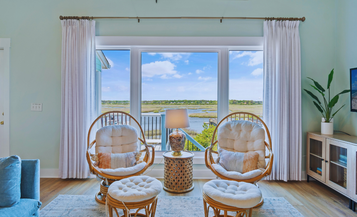 Living room at El Sol with rattan chairs, a round side table, and a window overlooking the marsh