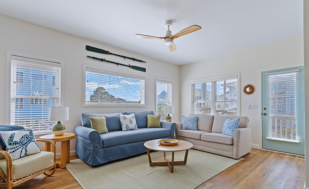 Bright living room at Sol Mar in Sunset Beach, North Carolina, with two sofas, a coffee table, and natural light from three windows.