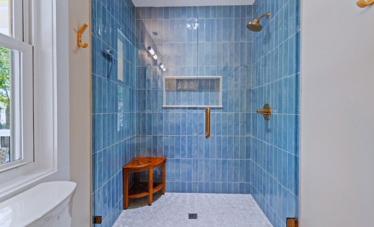 Bathroom at El Sol with a blue-tiled glass door walk-in shower, brass showerhead, and wooden stool.