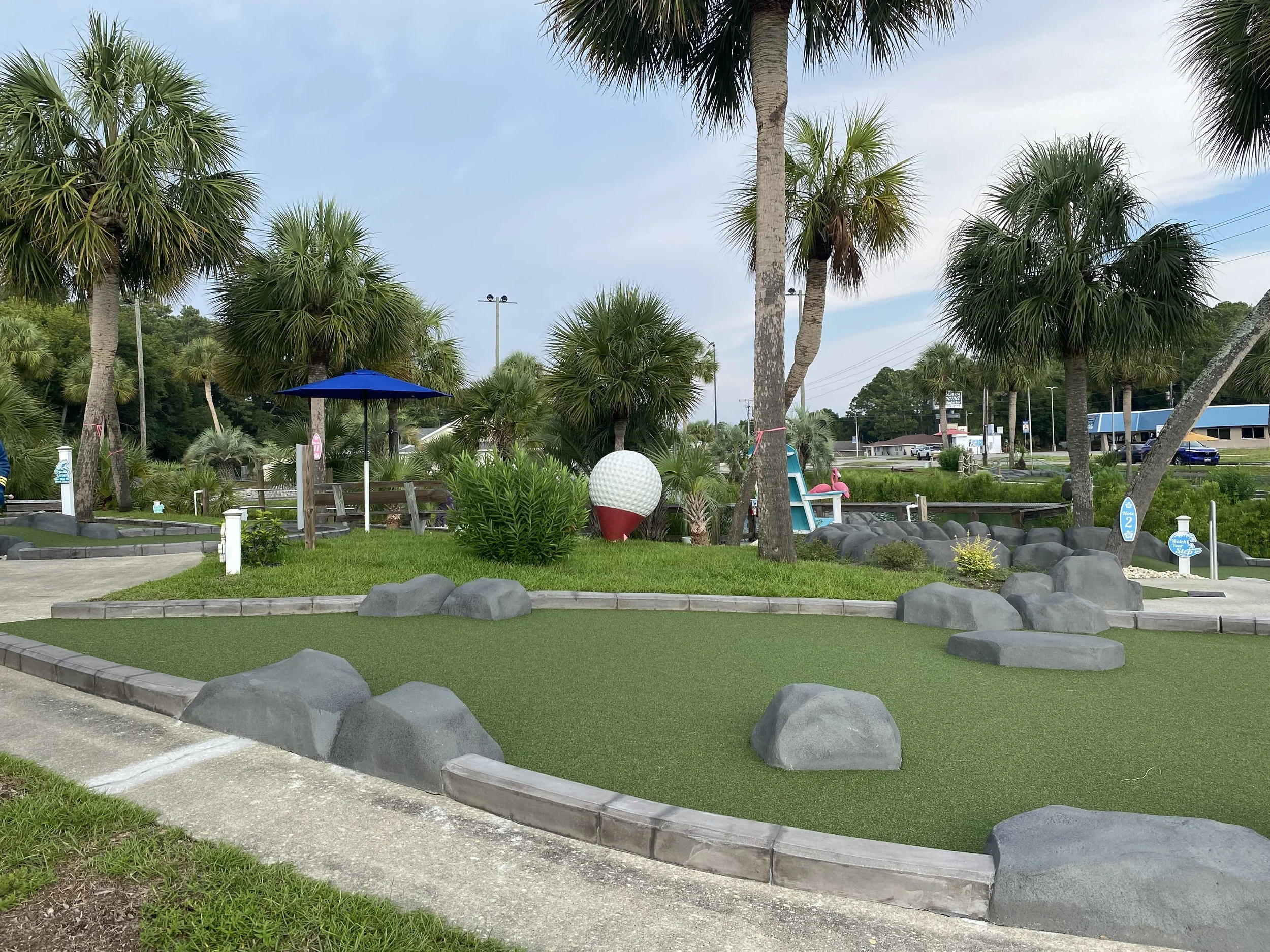 Mini golf course with artificial turf, large rocks, and palm trees.
