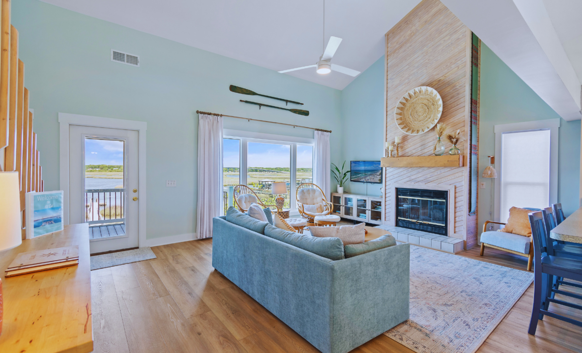 Living room at El Sol with a blue sofa, fireplace, and a wide window overlooking the tidal marsh.