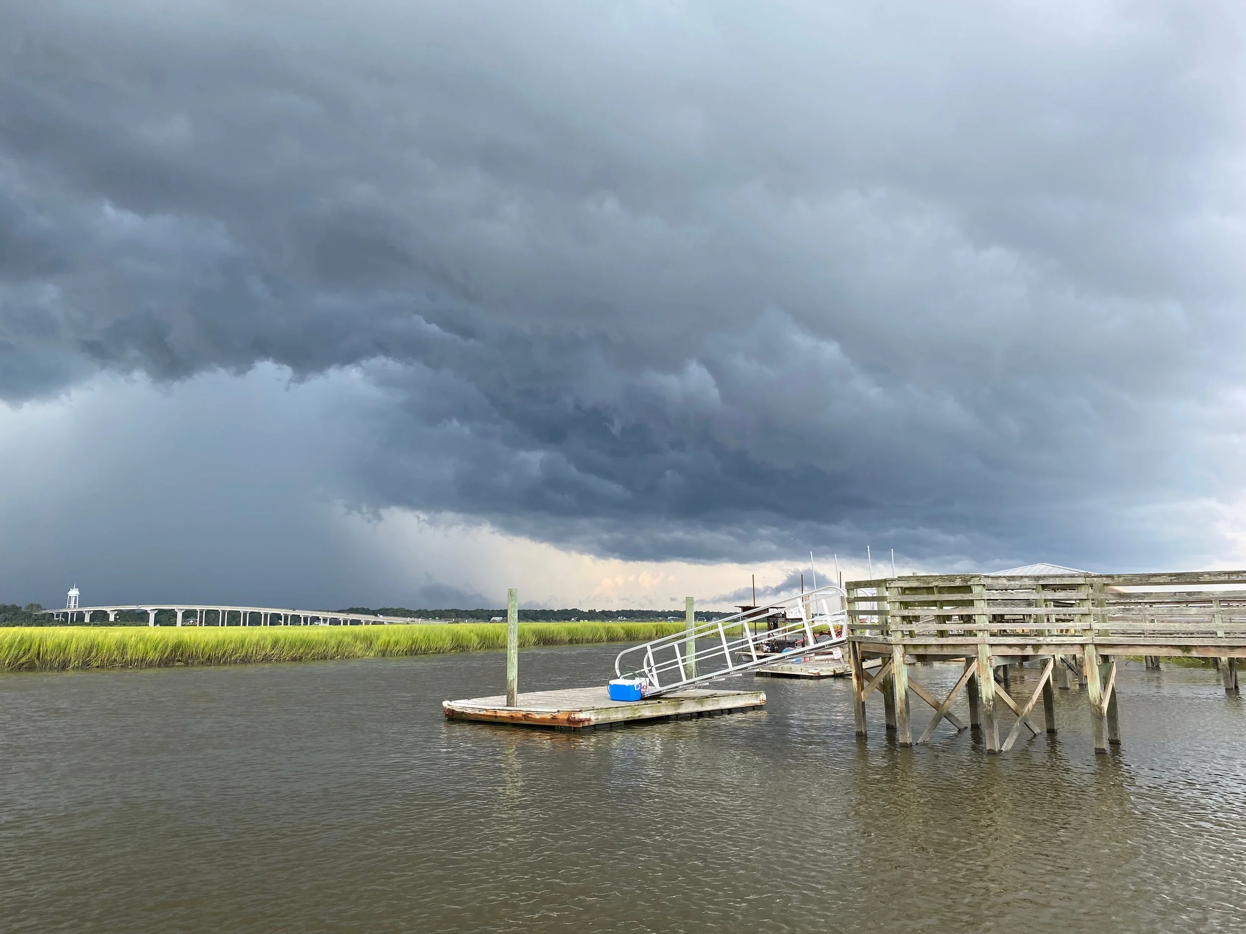 Stormy sky at the El Sol dock looking over a tidal marsh, and Sunset Beach bridge in the distance.