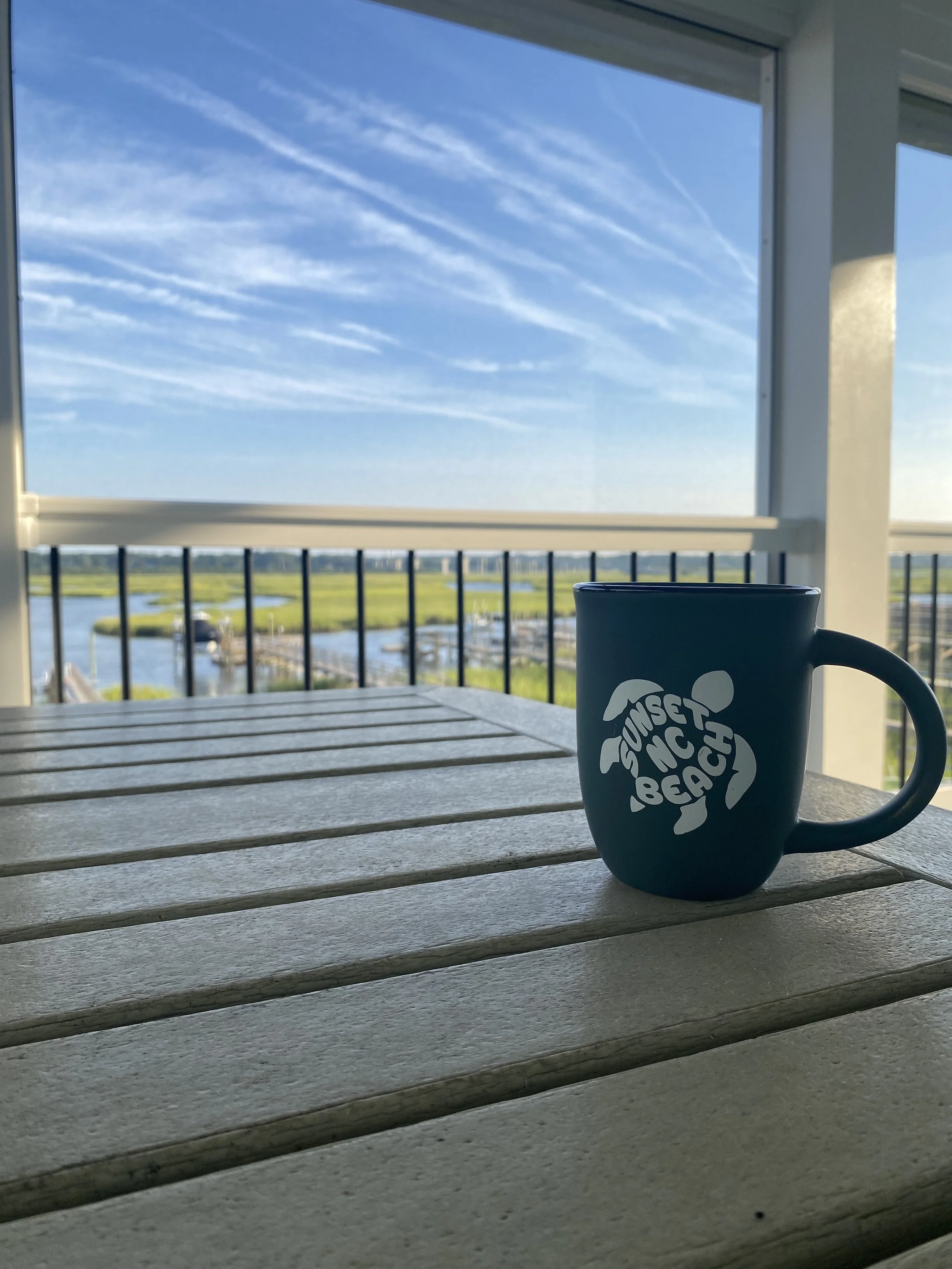 Blue 'Sunset Beach' mug on a table overlooking the marsh, from the Stay with Sol properties.