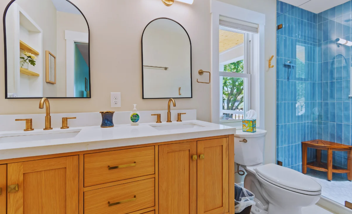 Bathroom at El Sol with double vanity sinks, gold fixtures, and a blue-tiled shower with a bench.