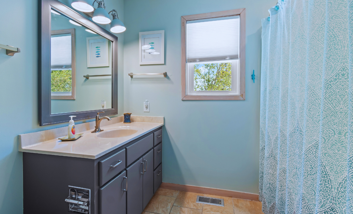 Bathroom at El Sol with a large mirror, light blue walls, and a shower curtain.