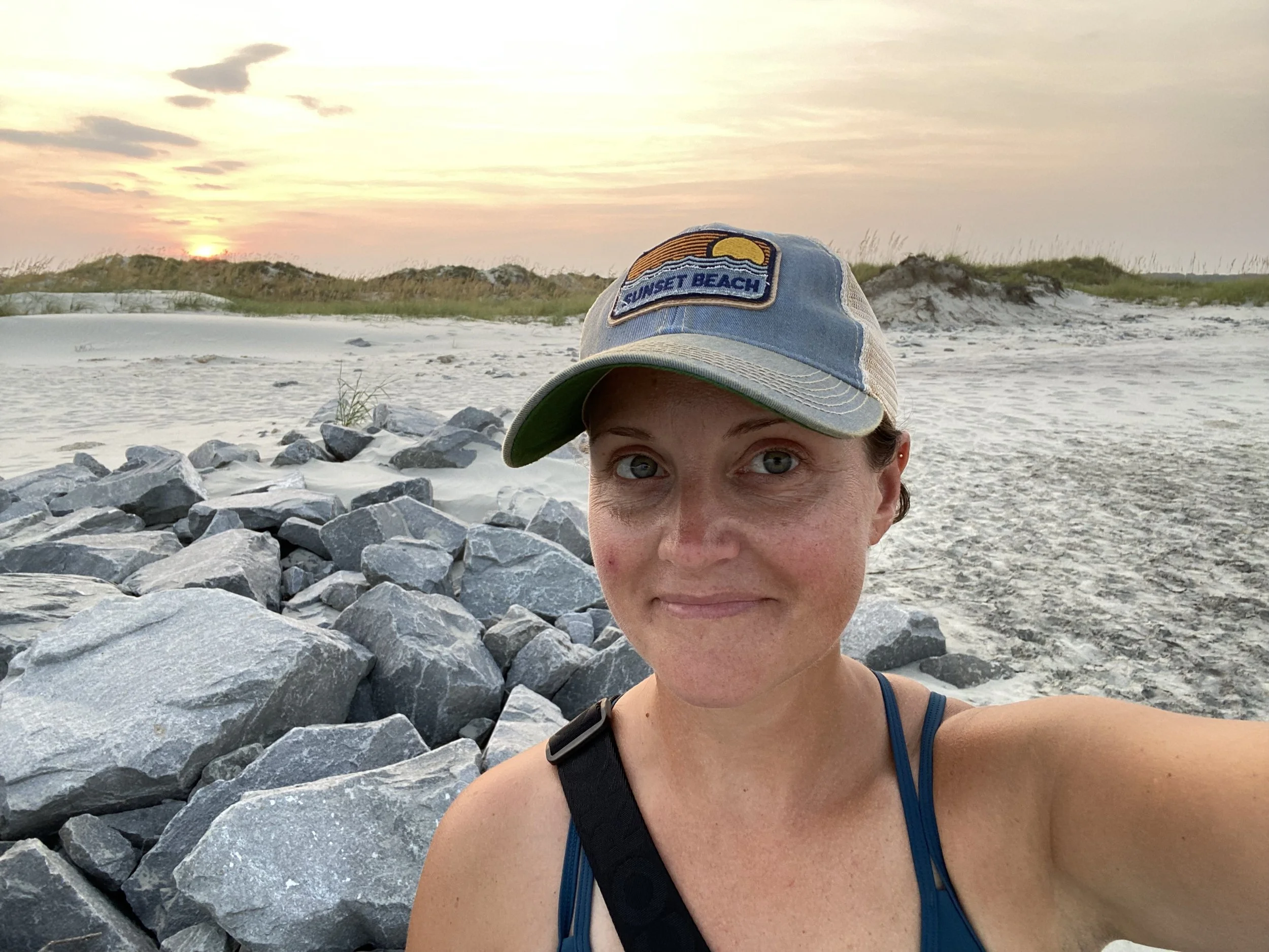 Kaleen wearing a Sunset Beach cap, standing on the rocks at the jetty during sunset