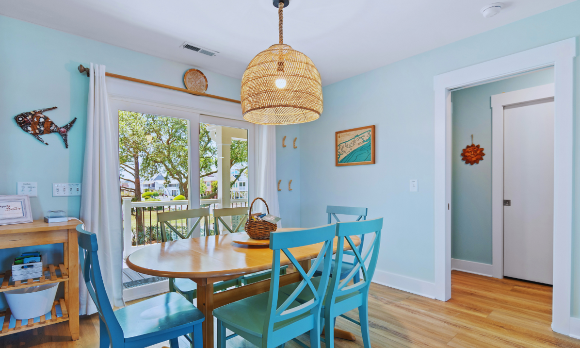 Dining room at El Sol with a wooden table, six blue chairs, and a sliding door to the covered front porch