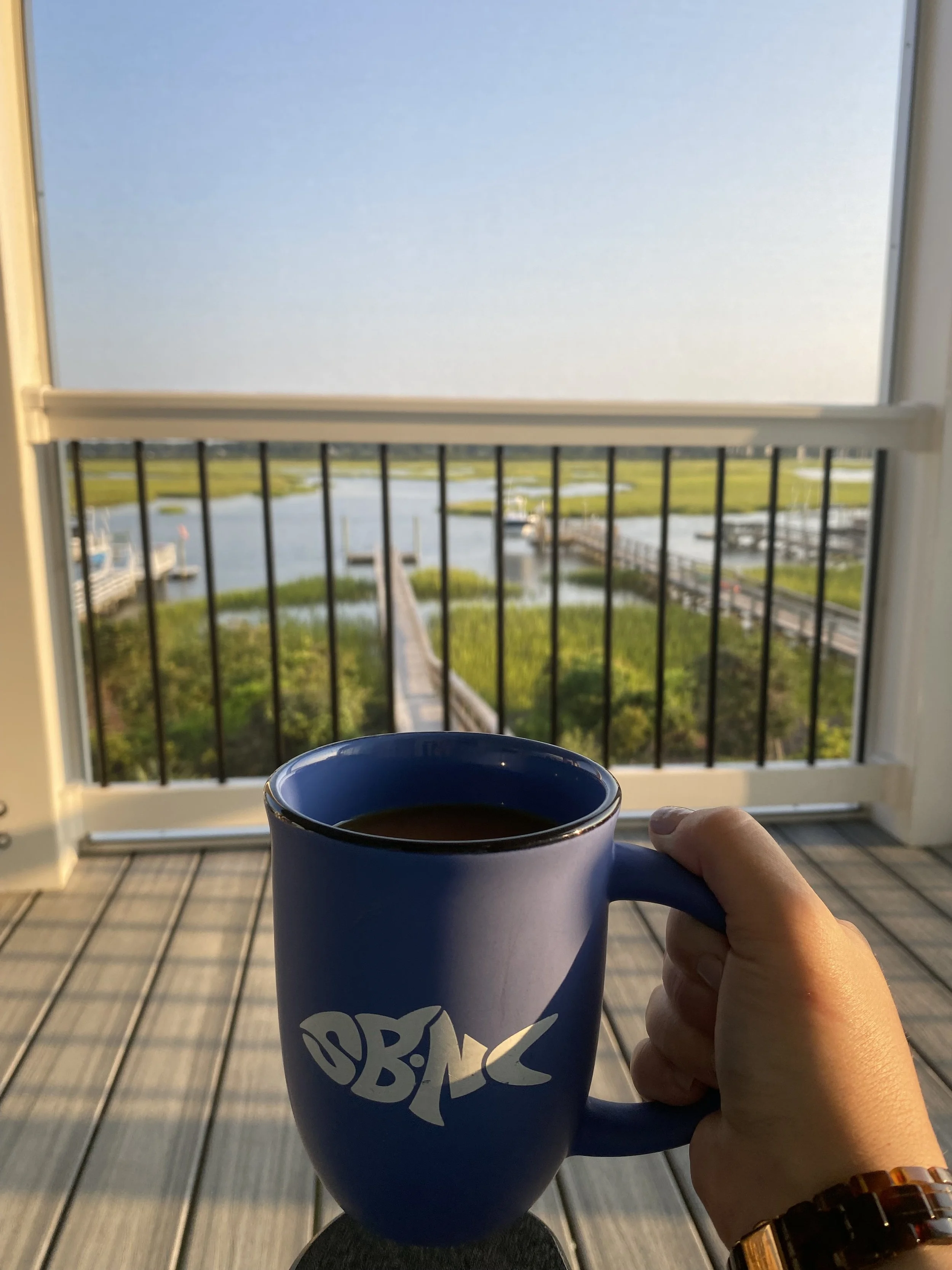 Holding a "SBNC" coffee mug on the balcony at El Sol, overlooking the dock and marsh.