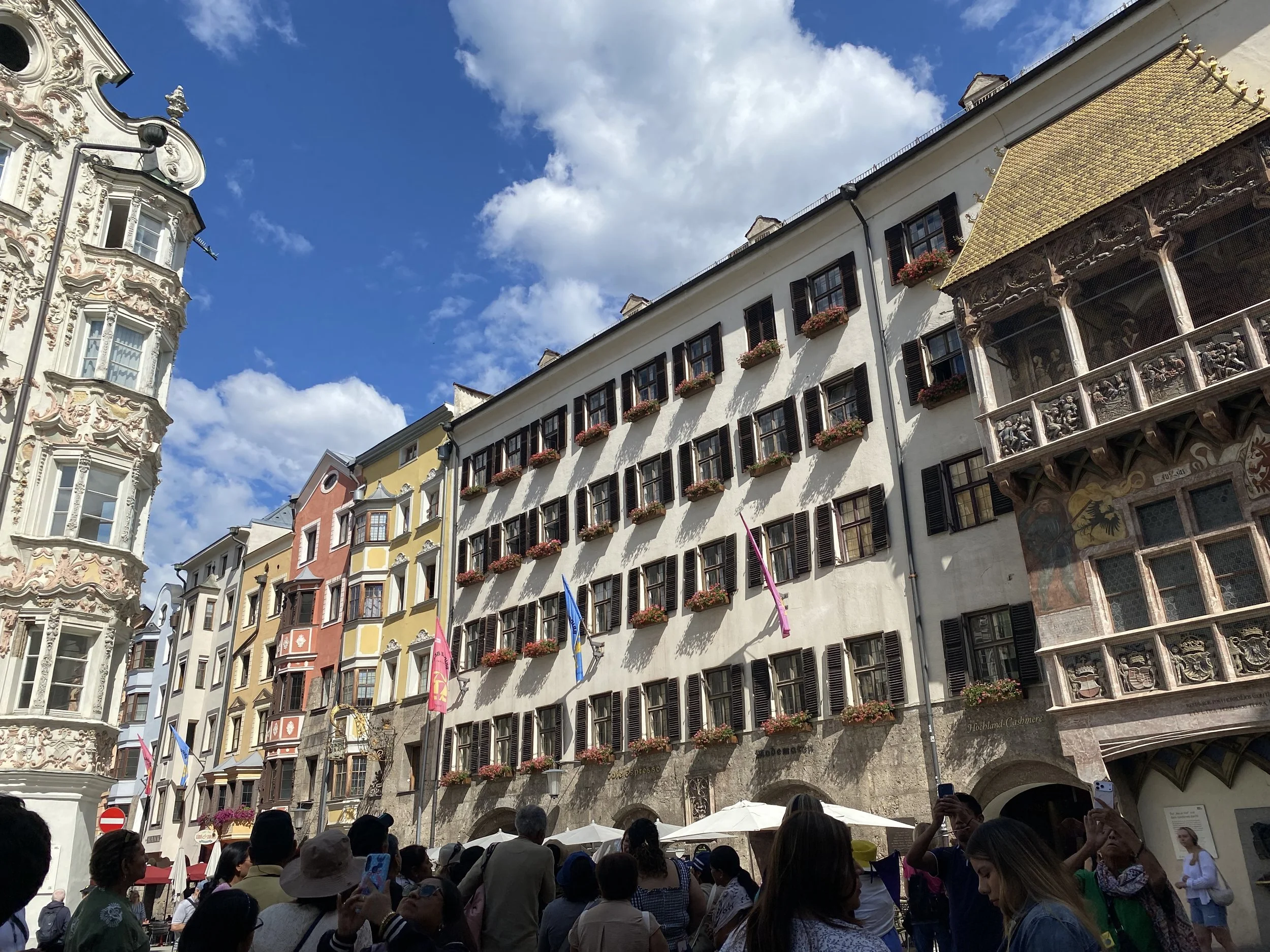 Colorful historic buildings and the Golden Roof with flower boxes at an outdoor market in Innsbruck, Austria."