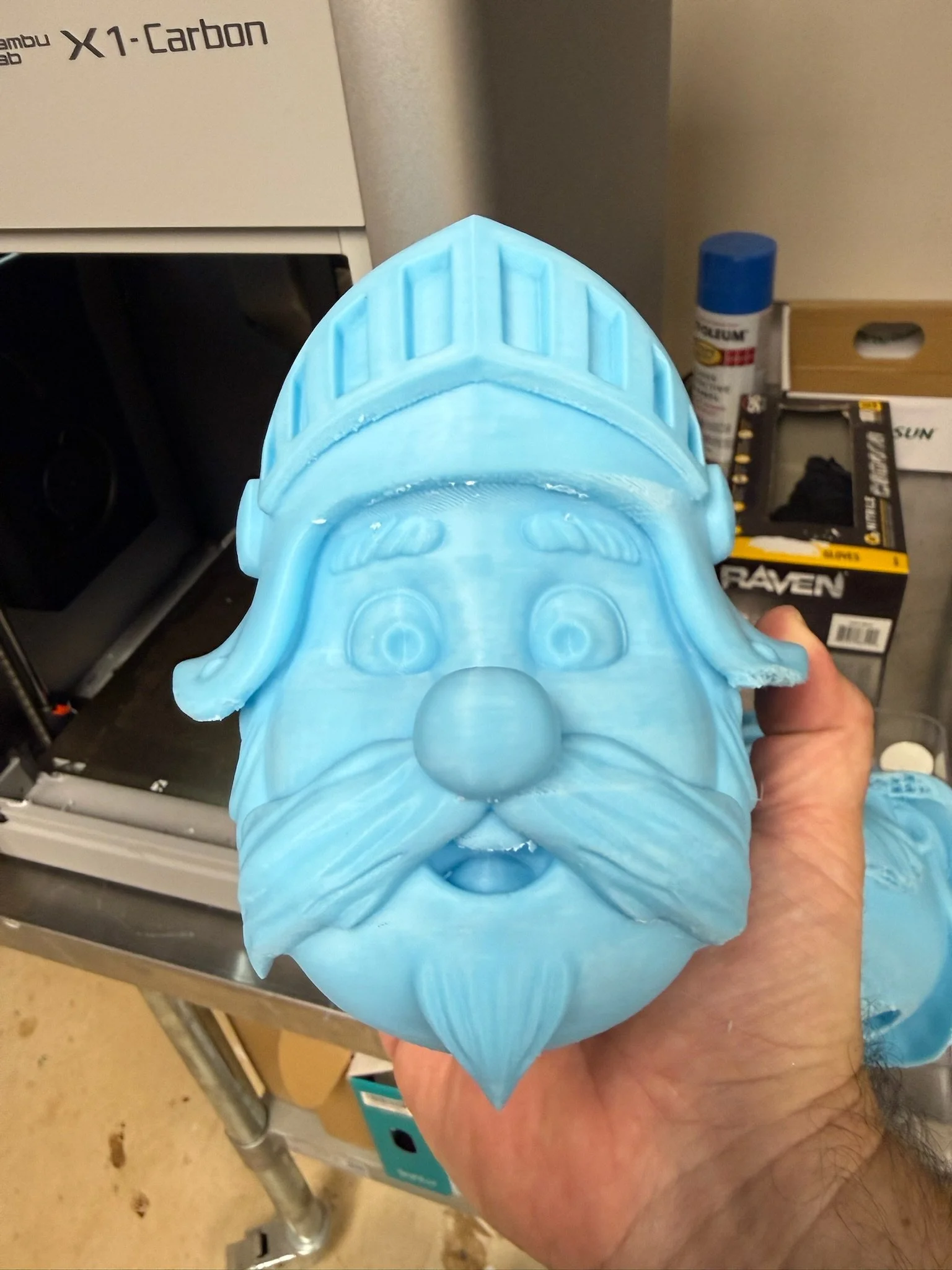 A blue plastic protective face shield with a cartoonish face, held by a person's hand.