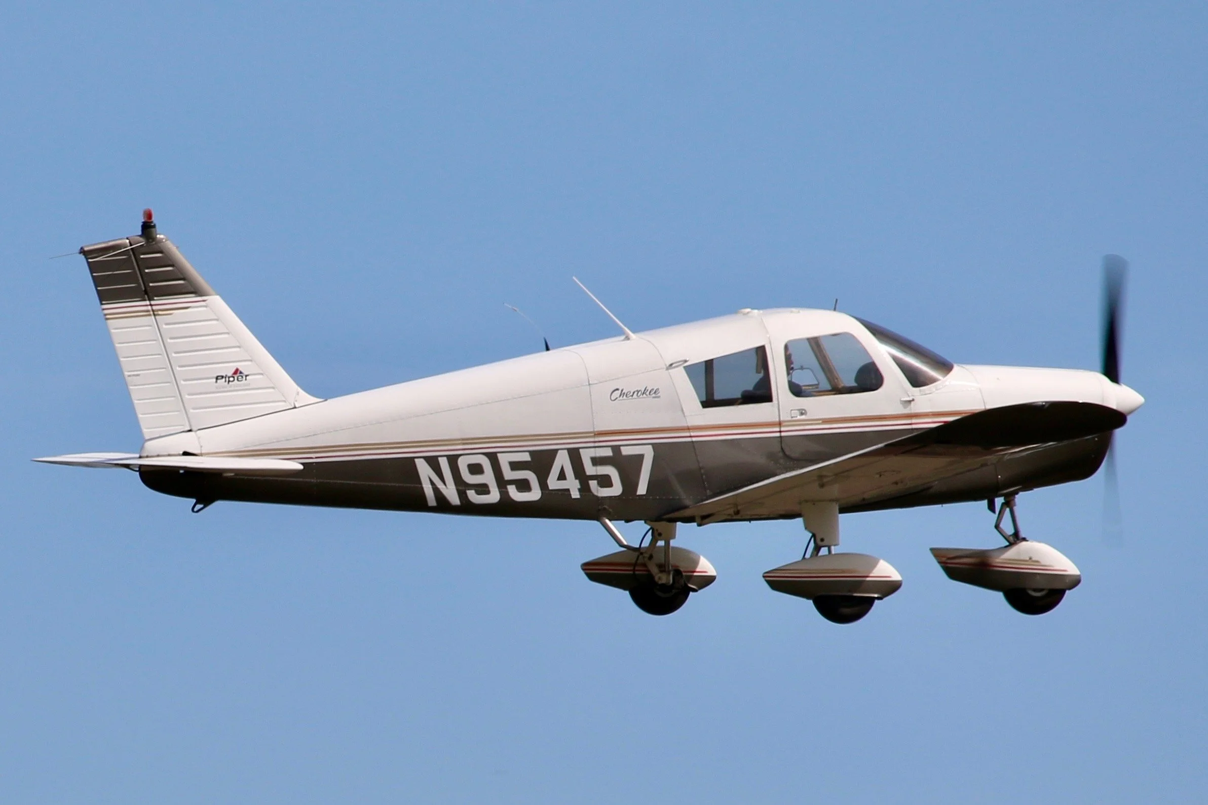 White Piper Cherokee airplane flying in a clear blue sky.