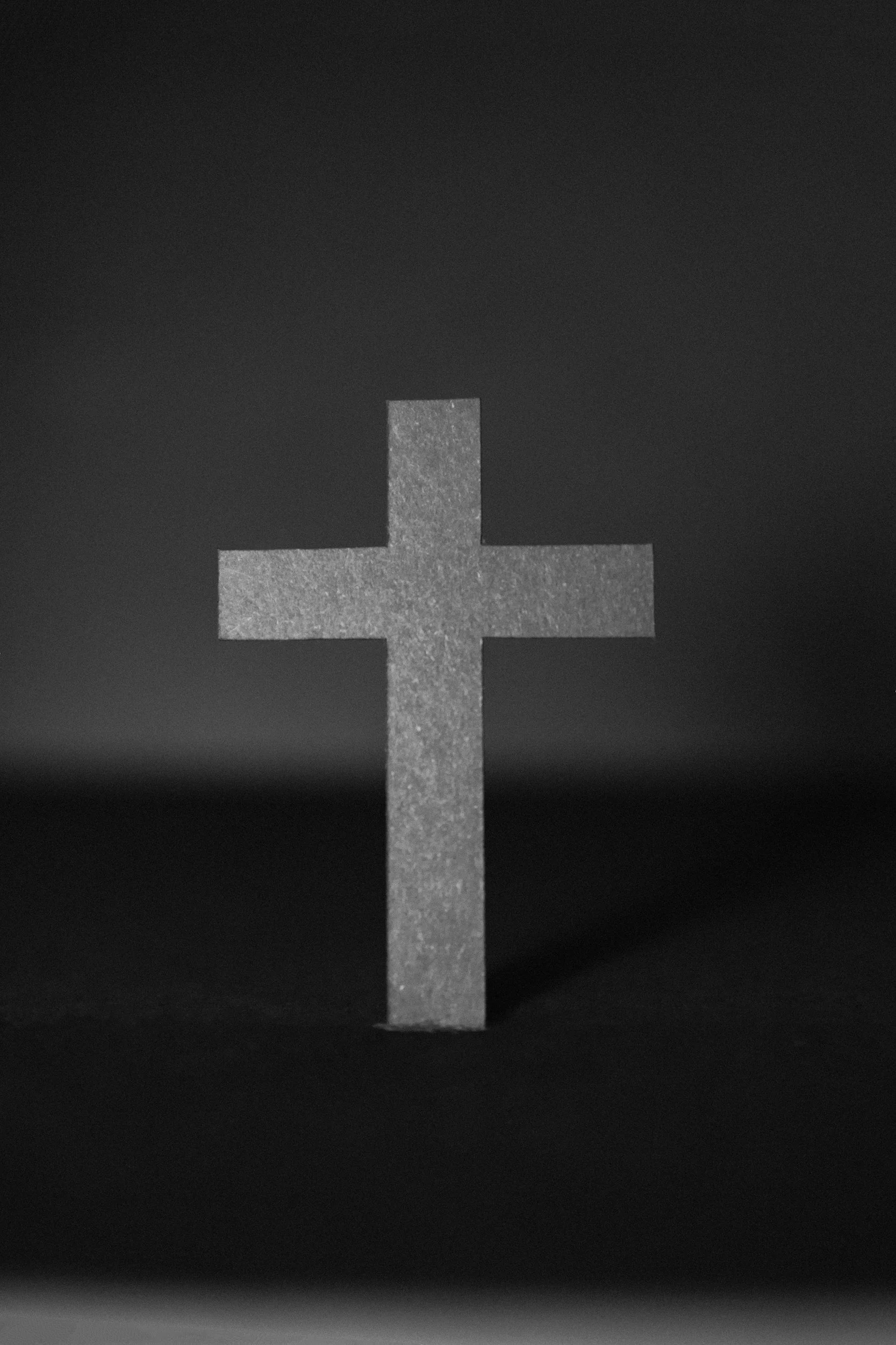 A metallic cross monument against a dark sky, with the lower part of the image blurred.