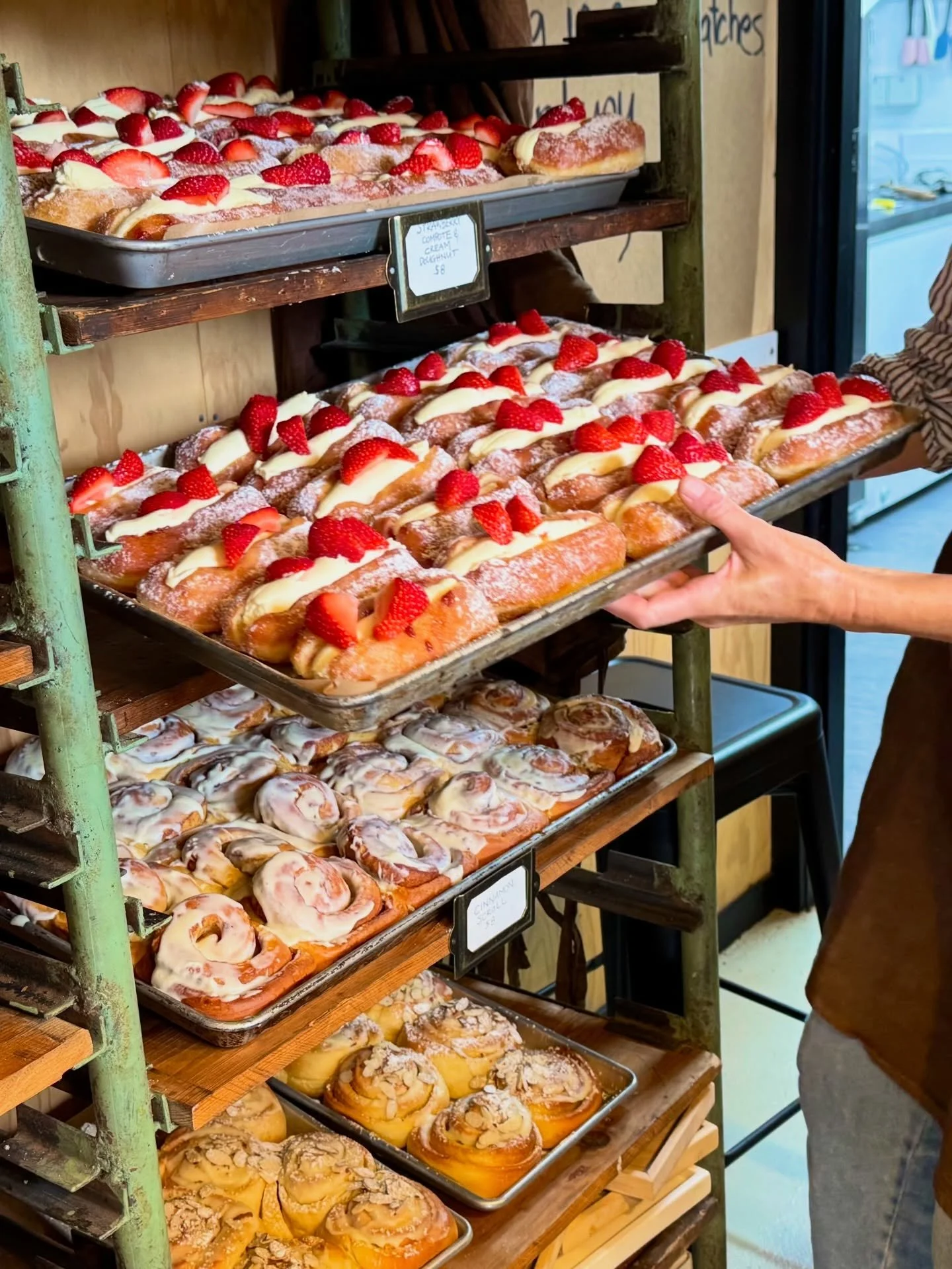 Tray of strawberry-topped éclairs on a bakery shelf, with additional pastries below.