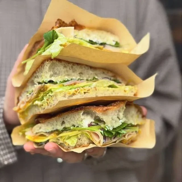 Focaccia sandwiches wrapped in STABLE, each filled with lettuce, tomato, cheese, and deli meats.