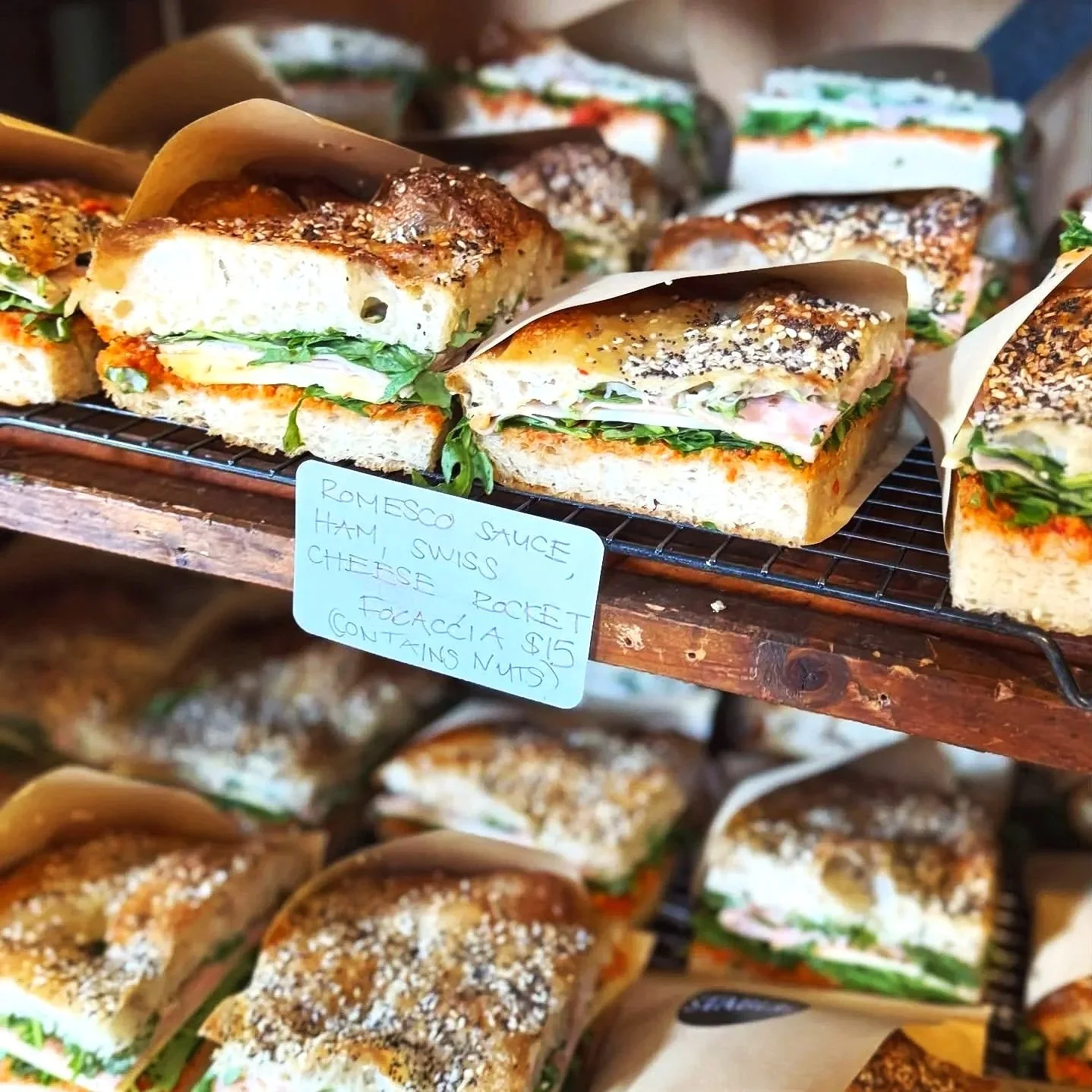 Assorted sandwiches with various meats, cheese, and lettuce on bread, labeled as Romesco sauce, ham, Swiss, cheese, rocket, and focaccia with nuts.
