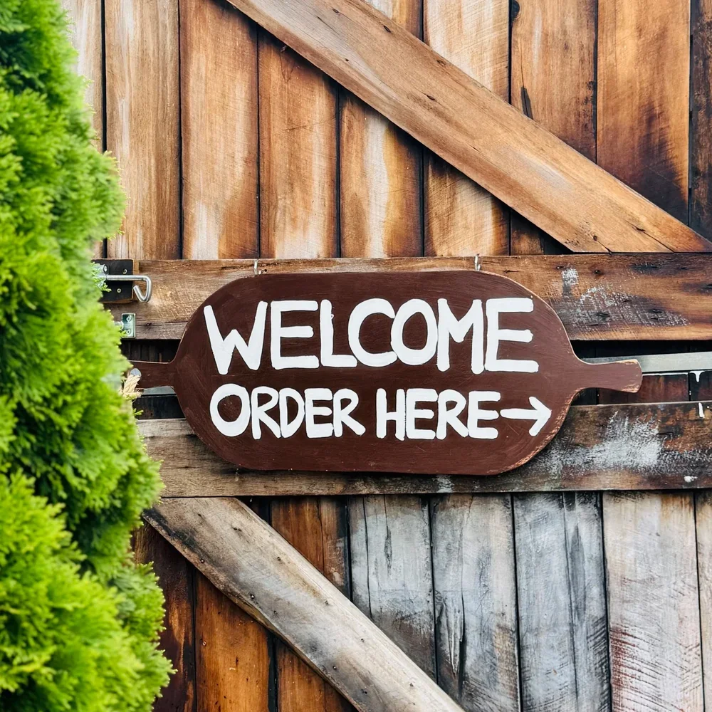 Wooden sign on a rustic wooden wall reading "Welcome, Order Here" at STABLE Greytown.