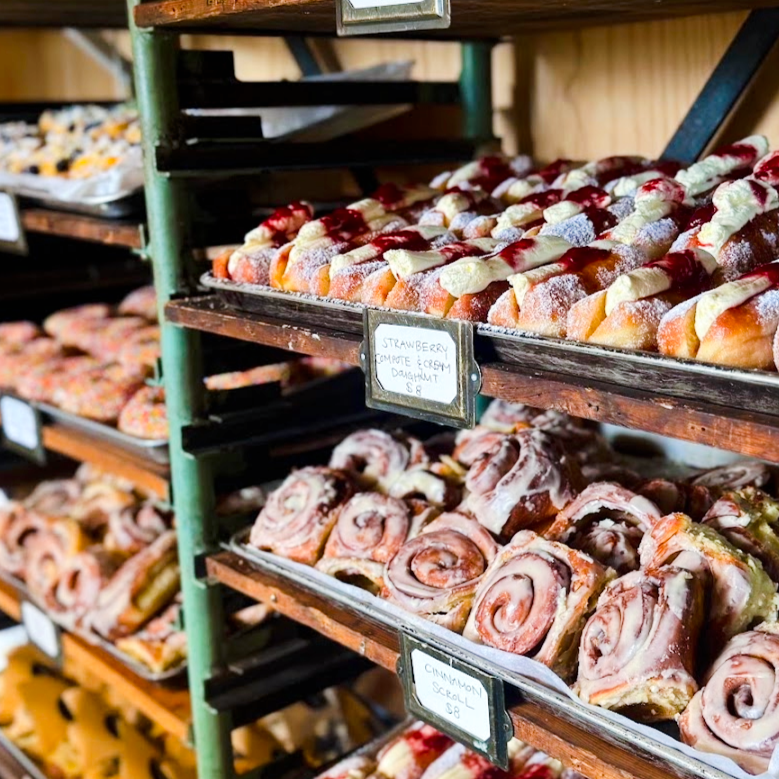 Display of glazed doughnuts topped with white icing and fruit preserves on a bakery rack, with a label indicating strawberry, caramel, and cream doughnuts.