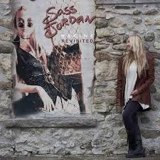 Woman leaning against a stone wall next to a large poster of a person wearing sunglasses and a leopard print jacket. Sass Jordan