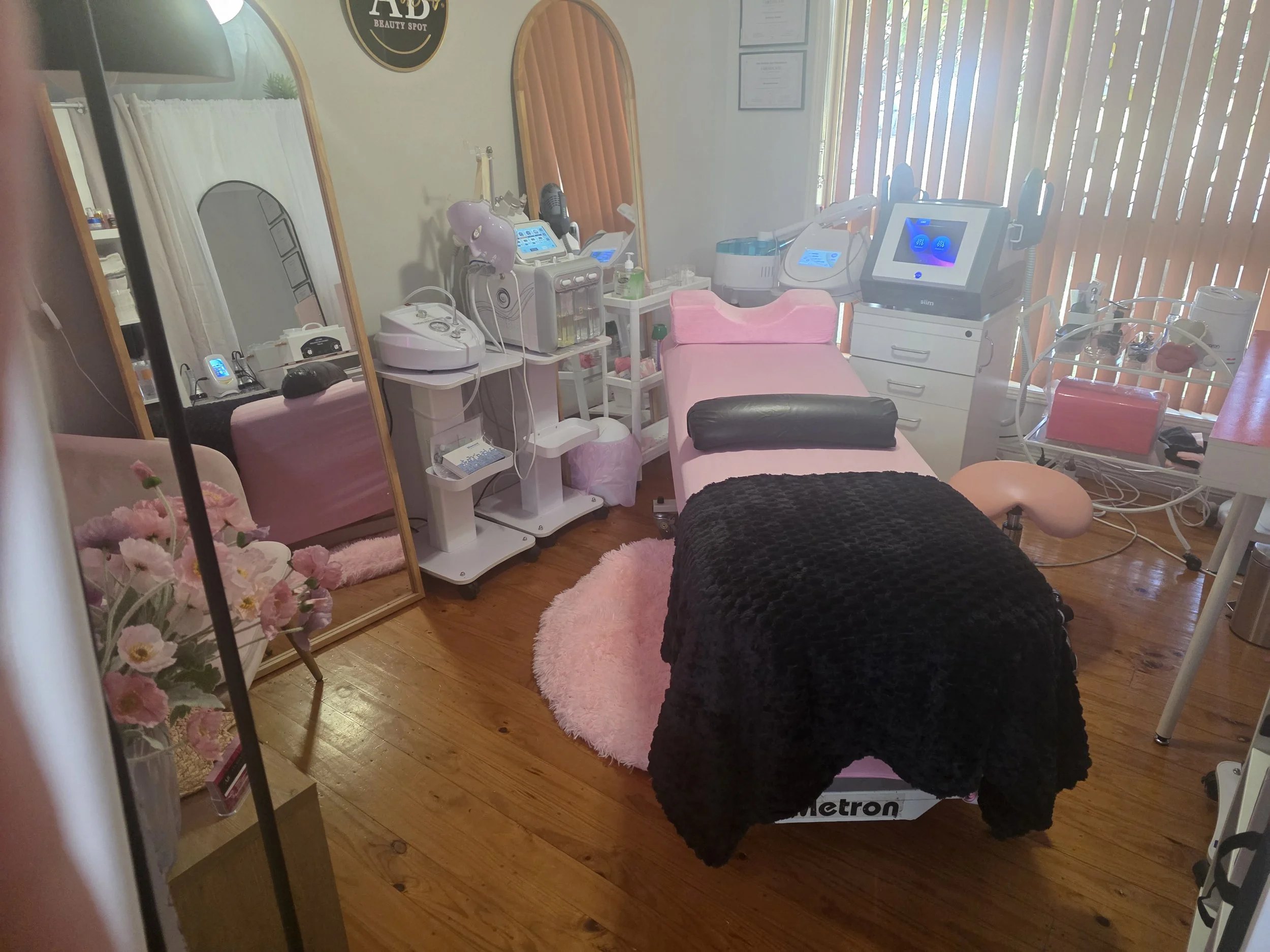 Beauty treatment room with treatment bed, equipment, mirrors, and floral decor.