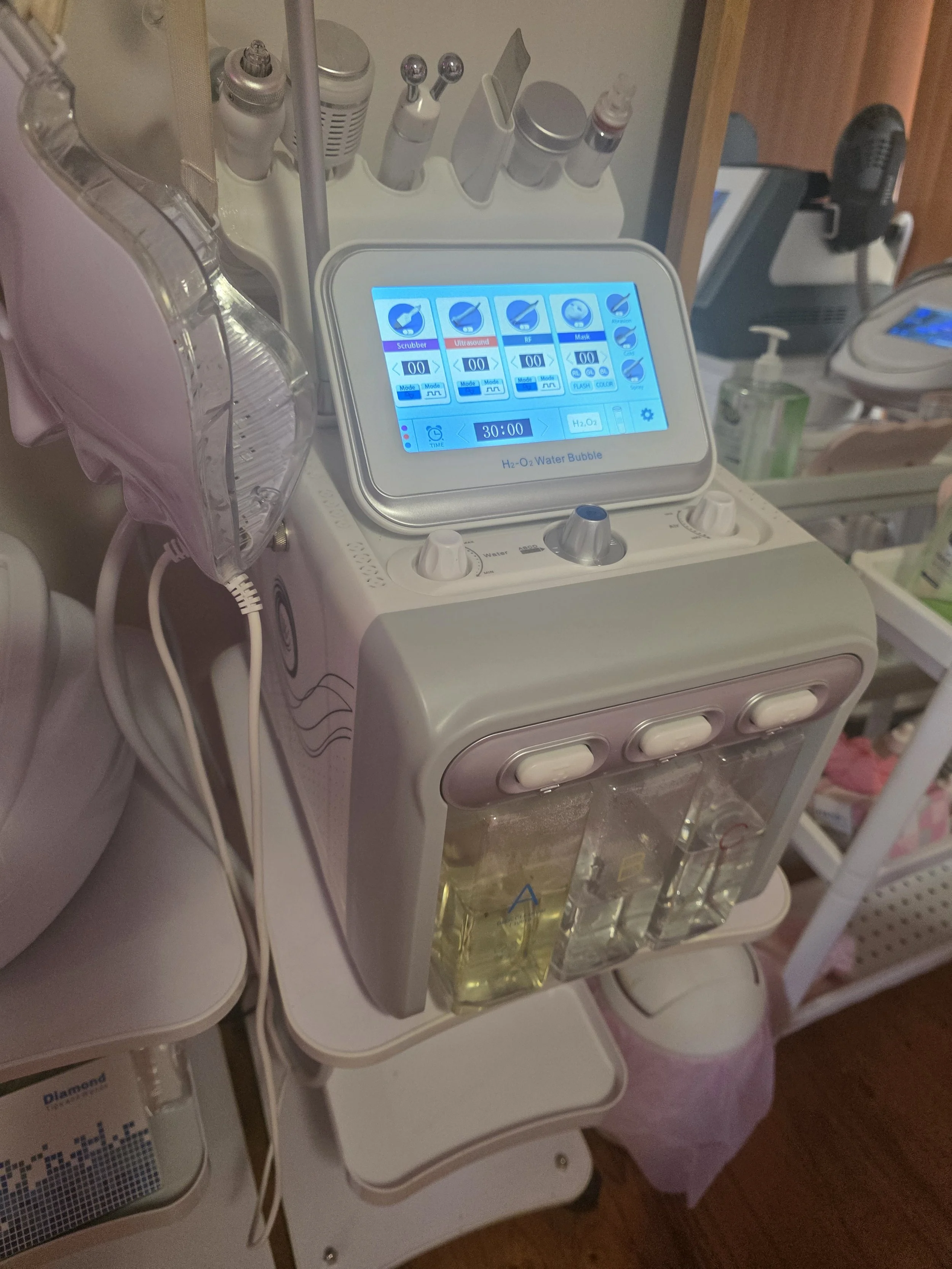 Medical device labeled H2-O2 Water Bubble with a digital touchscreen display, positioned on a stool in a clinical setting, with various medical supplies around it.