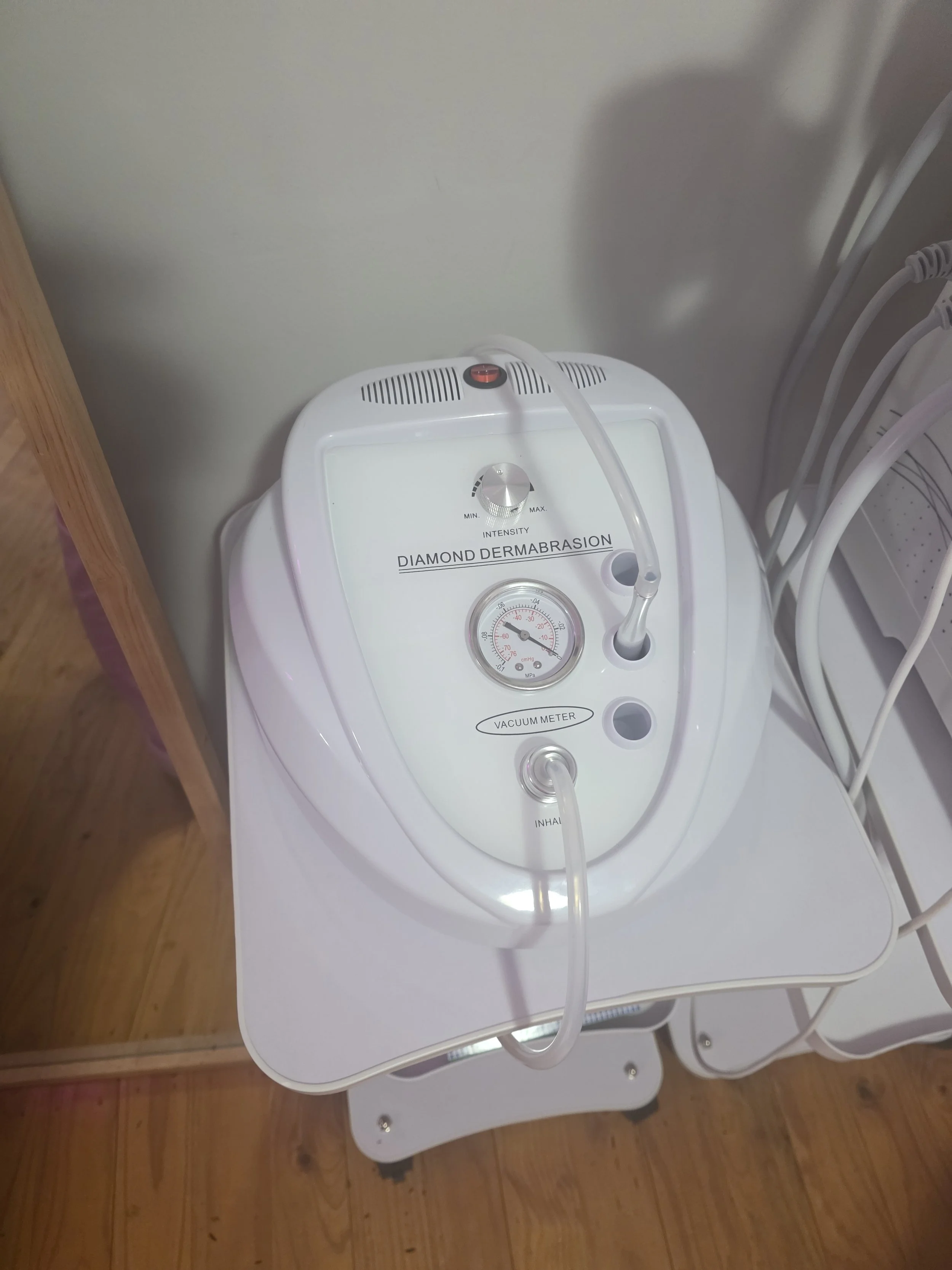 Device labeled 'Diamond Dermaabrasion' with a gauge, flexible tubes, and a control dial on a white table.