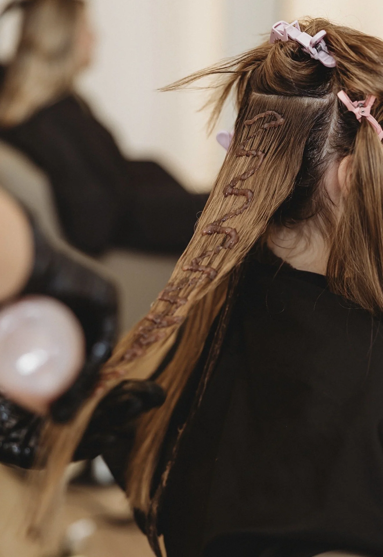 Close-up of a hairstylist sectioning a client's long brown hair with pink clips and adding decorative brown braids.