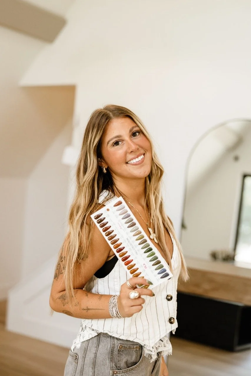 Smiling woman holding a chart of nail polish color samples in a bright salon
