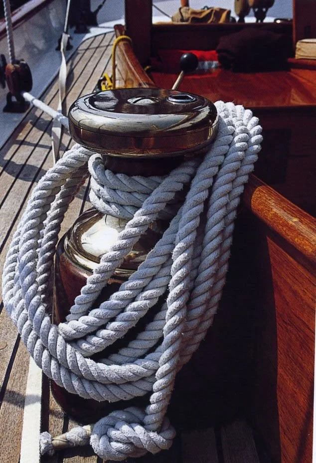 Close-up of a ship's winch with thick white rope coiled around it, mounted on the wooden deck of a boat.