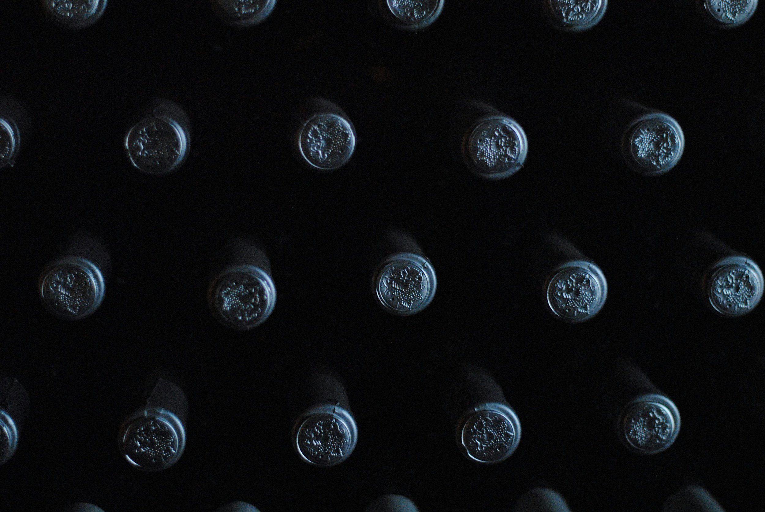 A close-up view of the top ends of caviar bottles arranged in a grid, showcasing their embossed metallic caps featuring intricate designs.