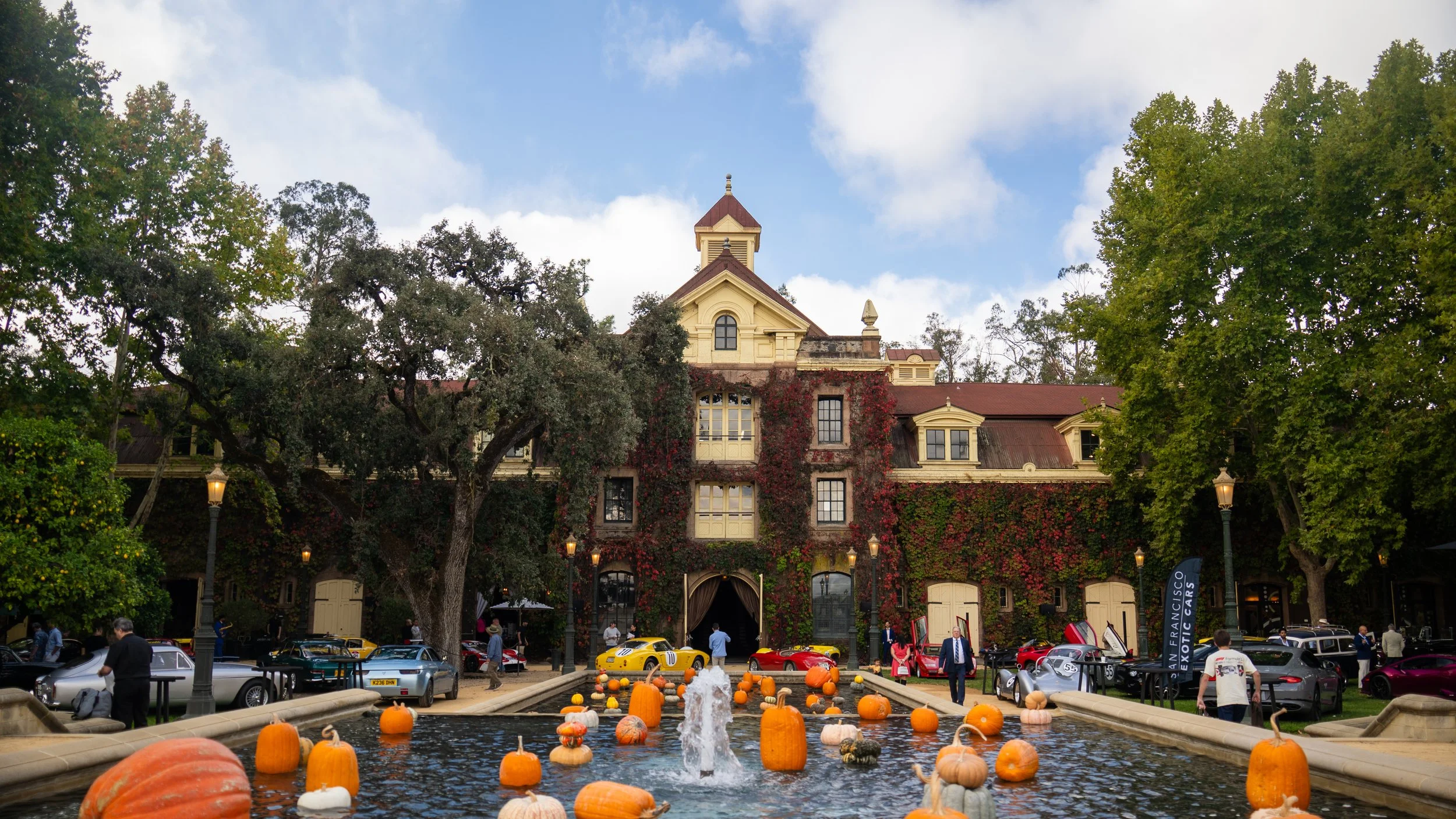 Historic building with ivy-covered walls, surrounded by trees and a fountain filled with pumpkins in an outdoor setting.
