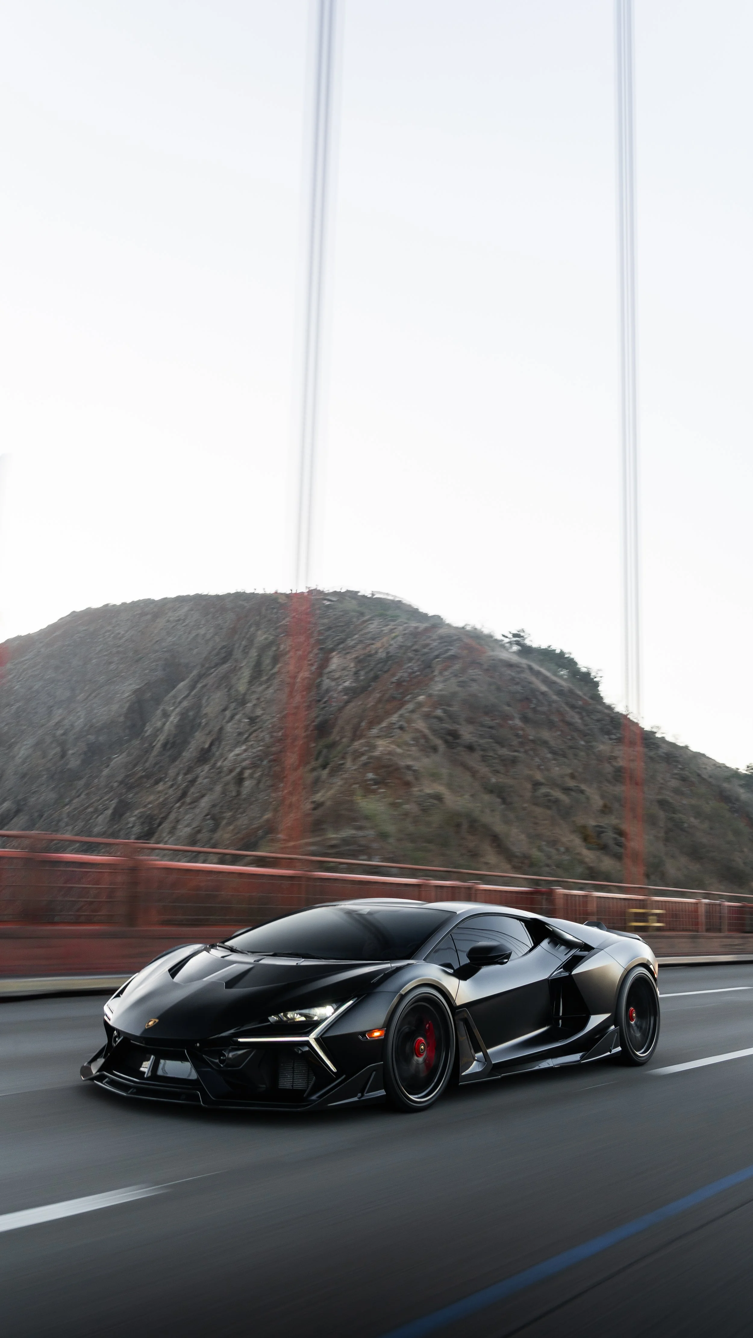A black sports car driving on a highway with a mountain and the Golden Gate Bridge in the background.