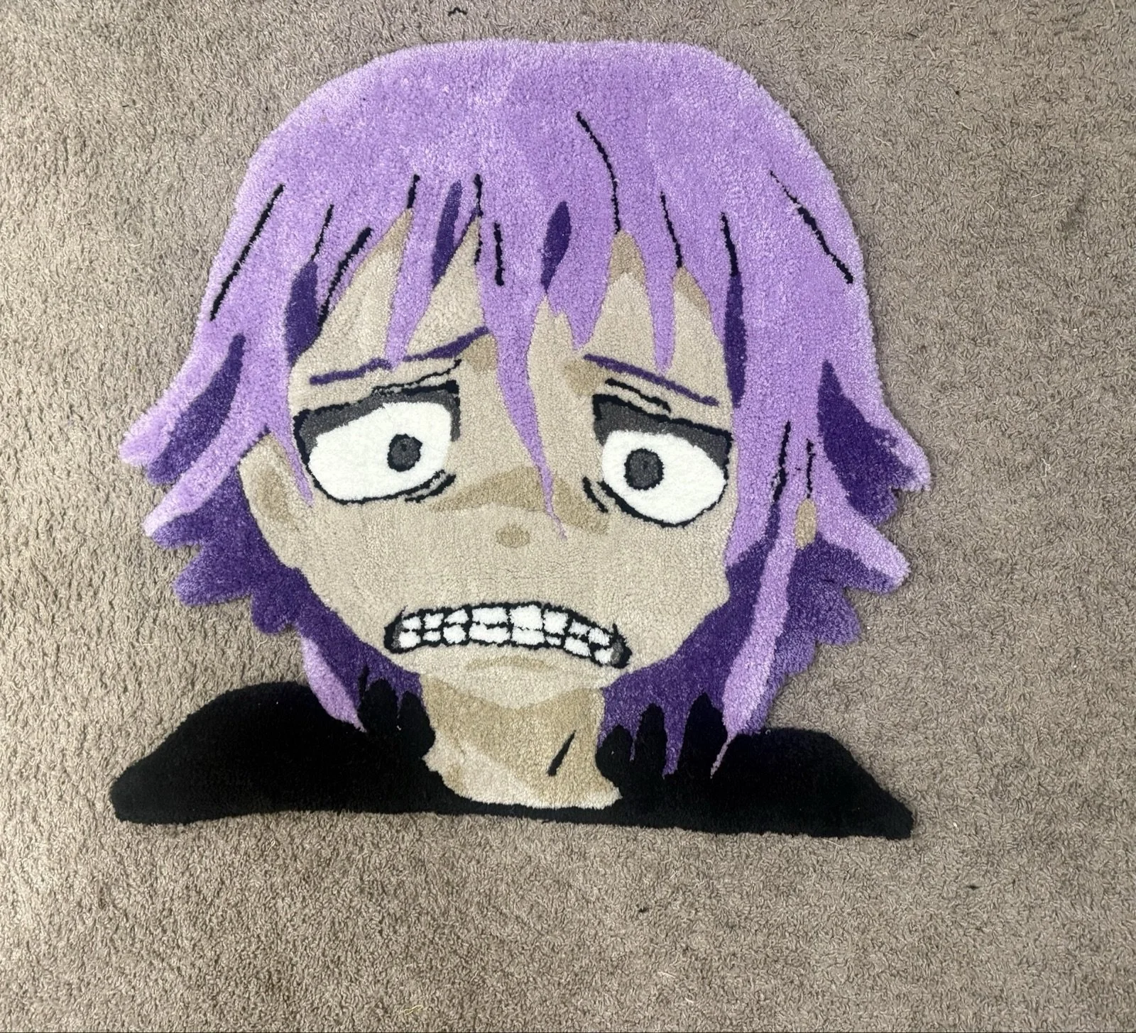 A face-shaped rug featuring an anime-style character with purple hair, wide eyes, and a distressed expression, placed on a beige carpet.