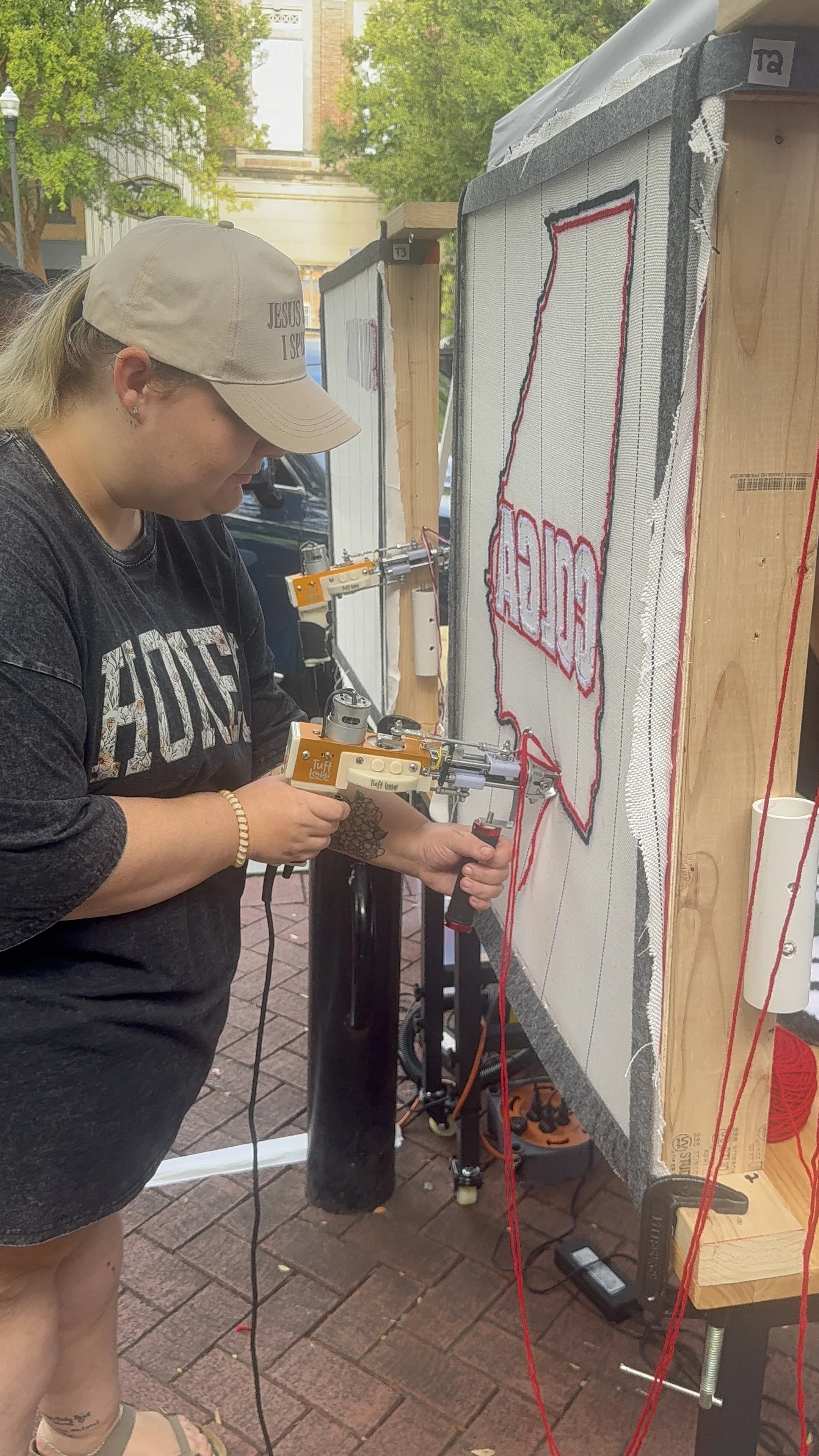 A woman working on a large sewing project outdoors, using a hot glue gun on a fabric with a red outline of a speech bubble.