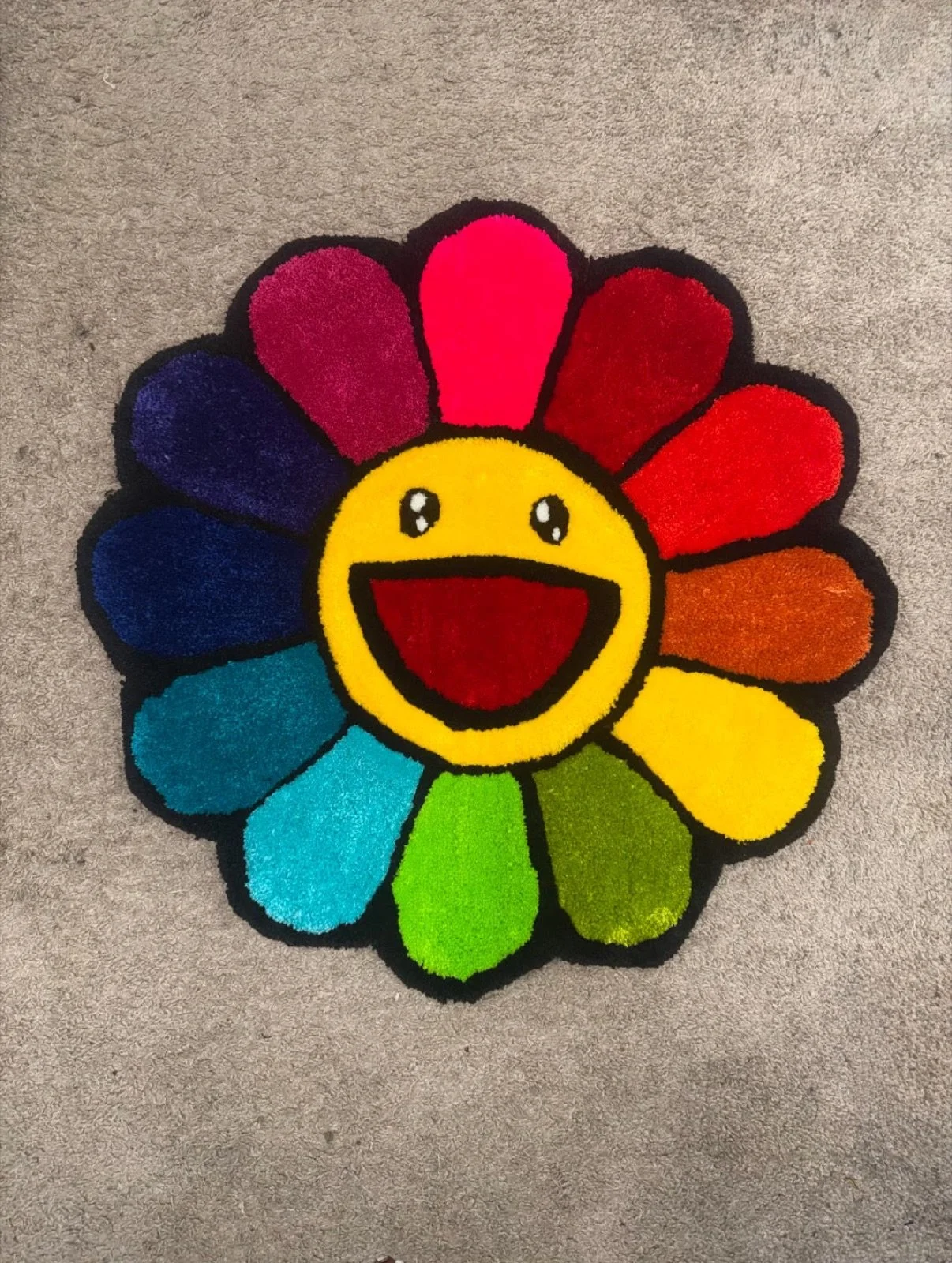 Colorful flower-shaped rug with a happy smiling face in the center, placed on a gray carpeted floor.