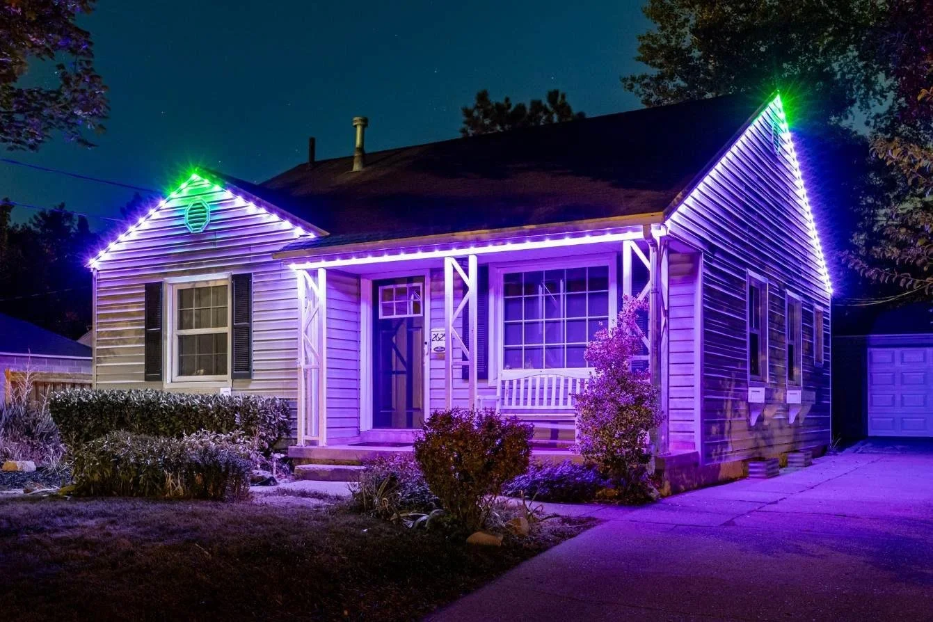 A house decorated with purple and green Christmas lights at night.