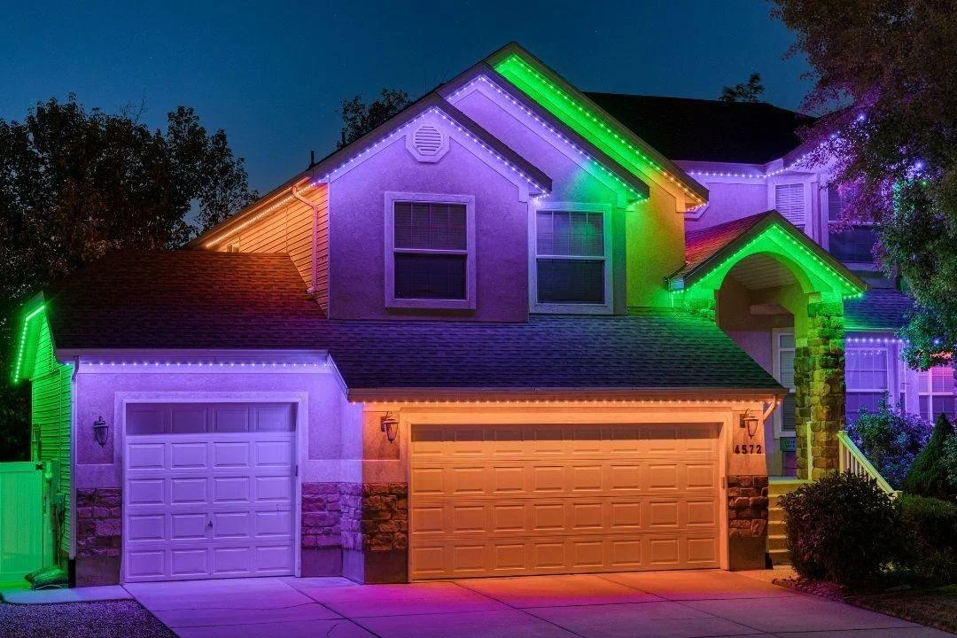 A two-story house decorated with colorful LED lights at night, with purple, green, orange, and white ánh sáng outlining the roof, windows, and garage.