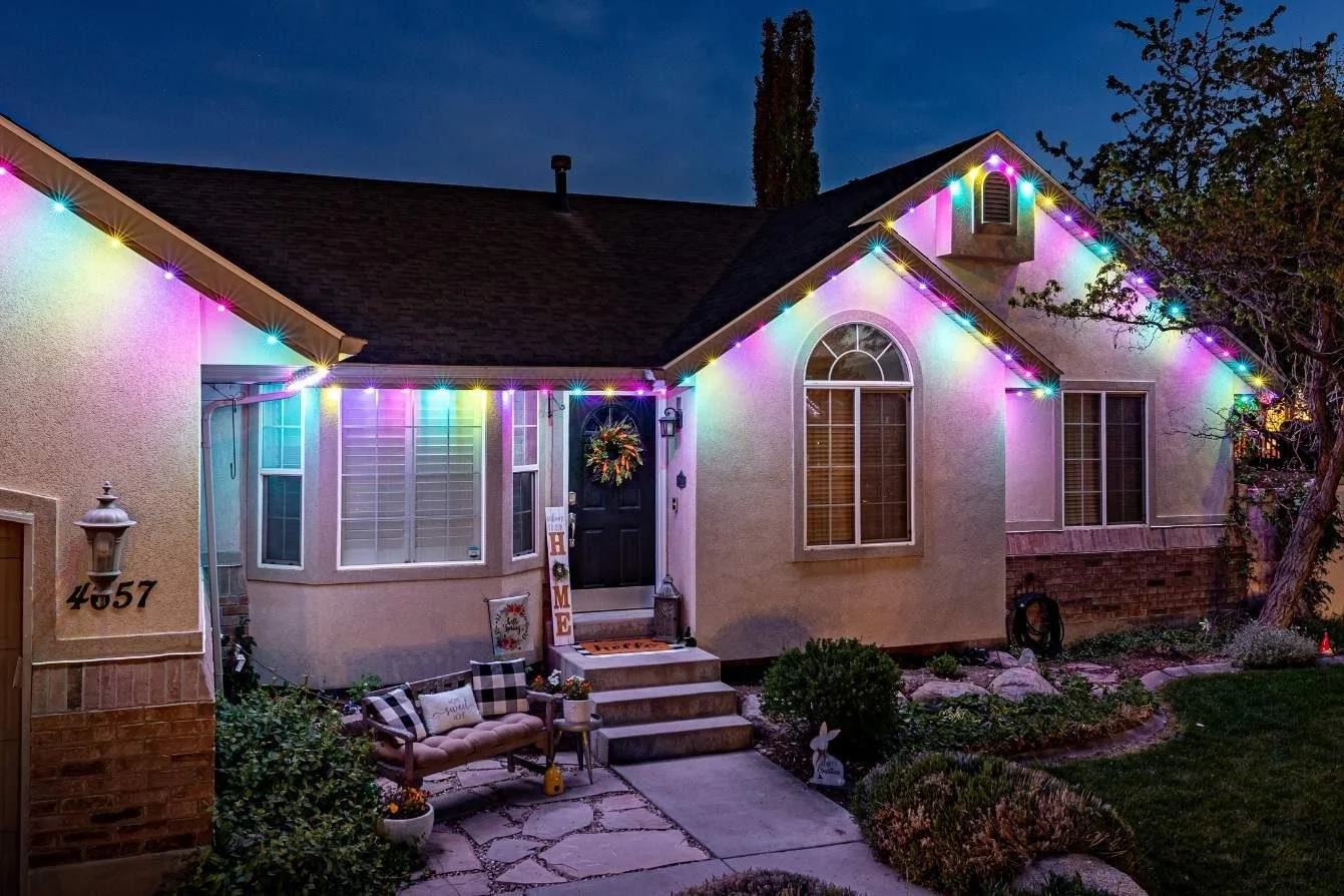 Front yard of a house decorated with colorful string lights at dusk.
